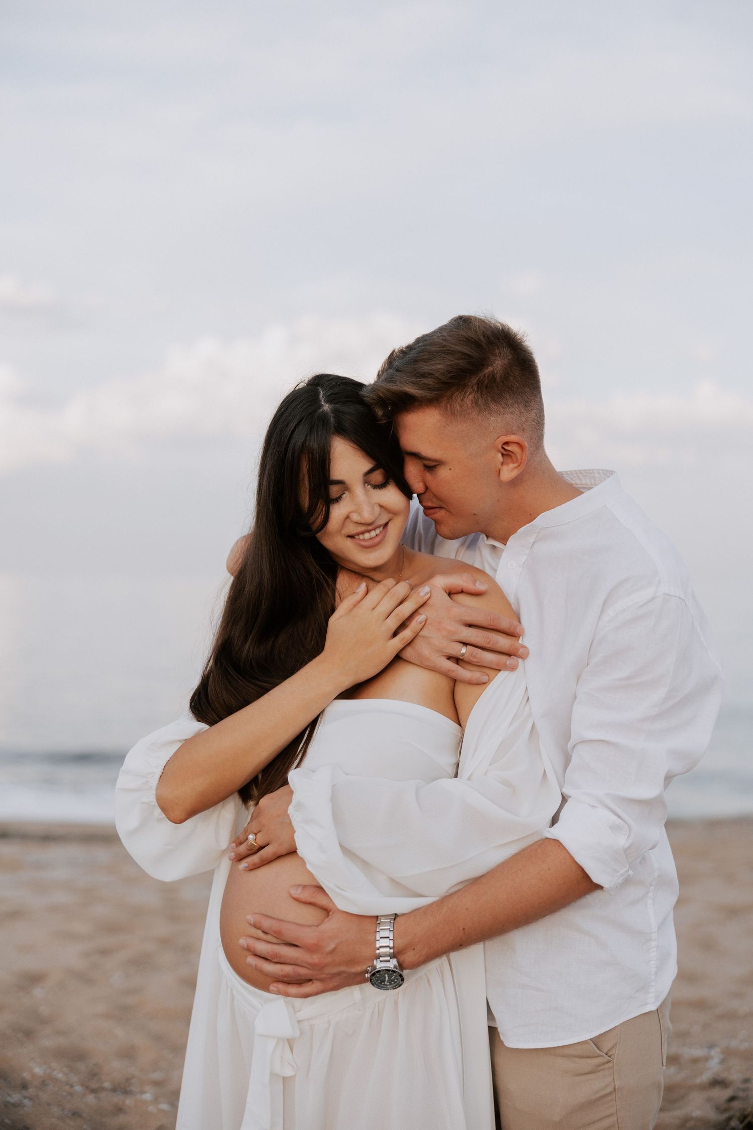 Intimate beach portrait of couple in white embracing.