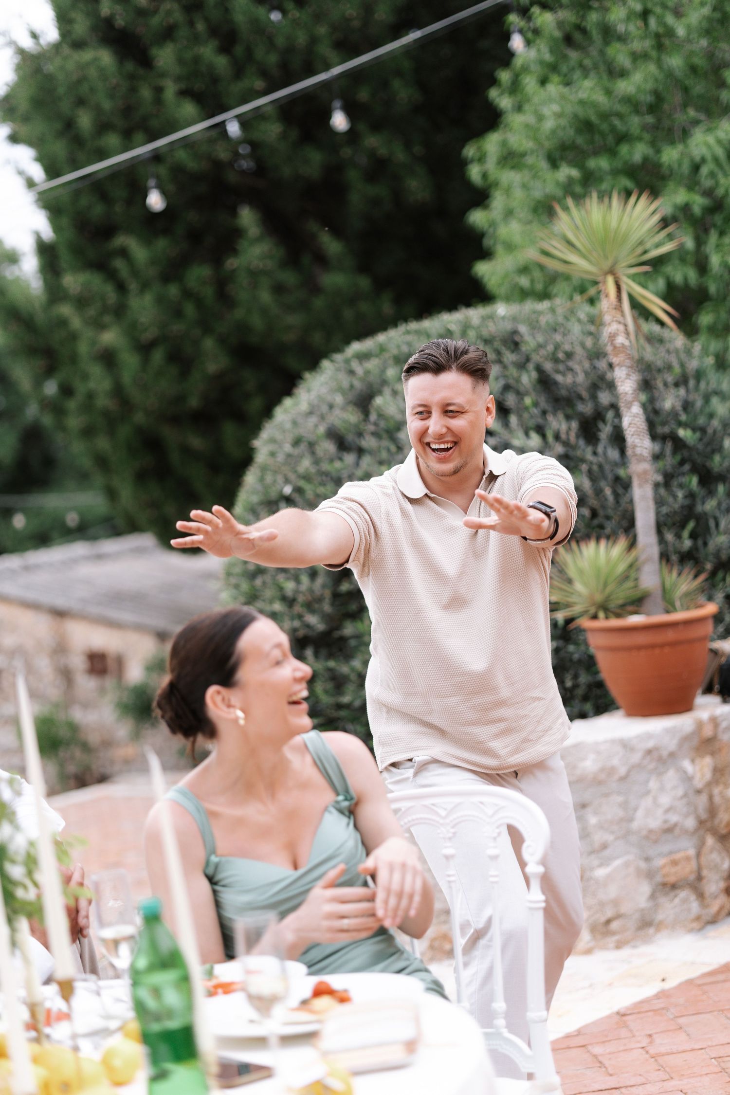 A joyful outdoor gathering with string lights and palm plants on a stone patio during a summer celebration.