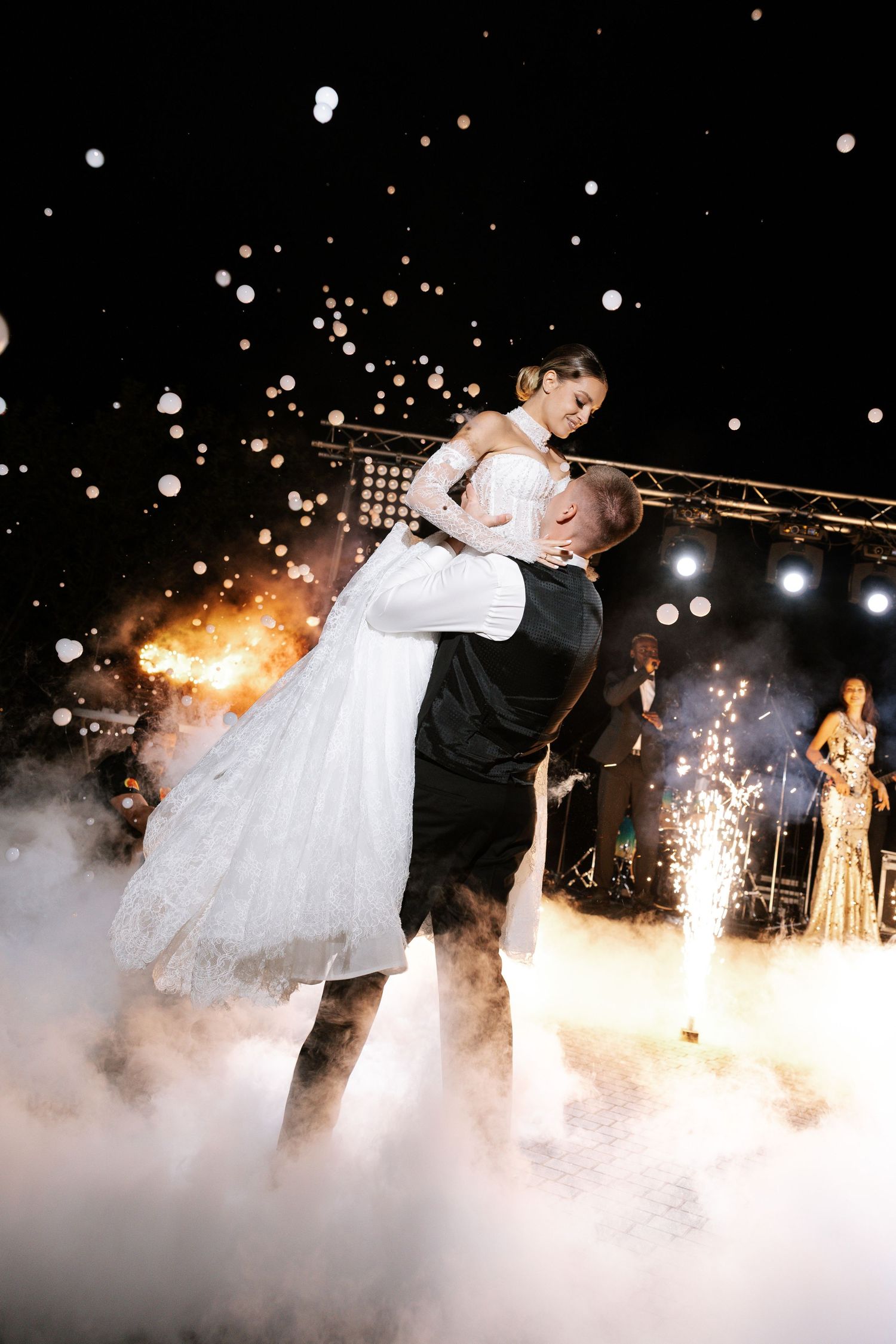Couple shares romantic dance moment surrounded by fog and sparklers during wedding reception celebration.