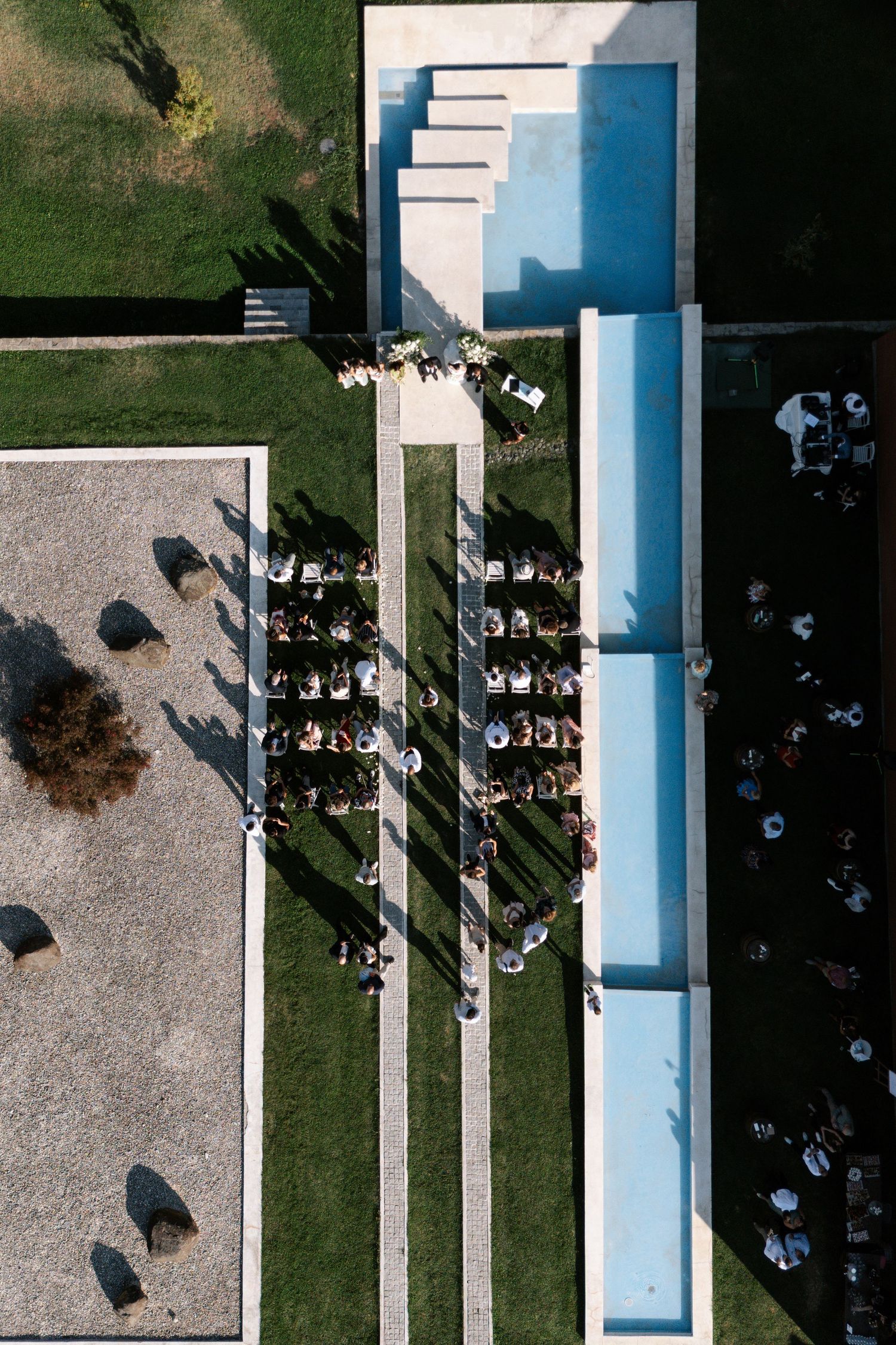 Aerial view of a modern building with white columns and walkways casting geometric shadows on concrete and grass.