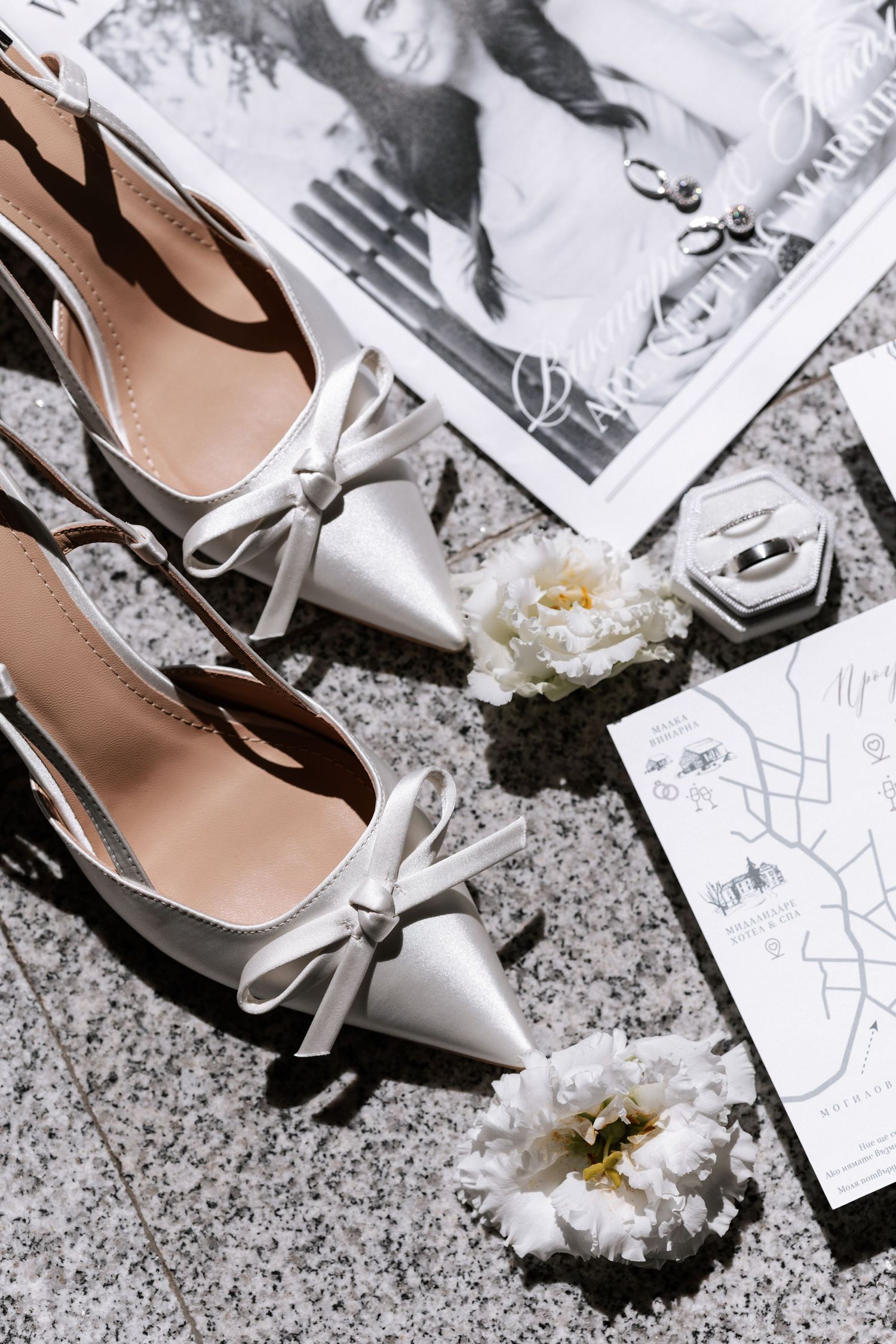 Elegant silver bow flats arranged with white peonies, a vintage photo, and a map on a granite surface.