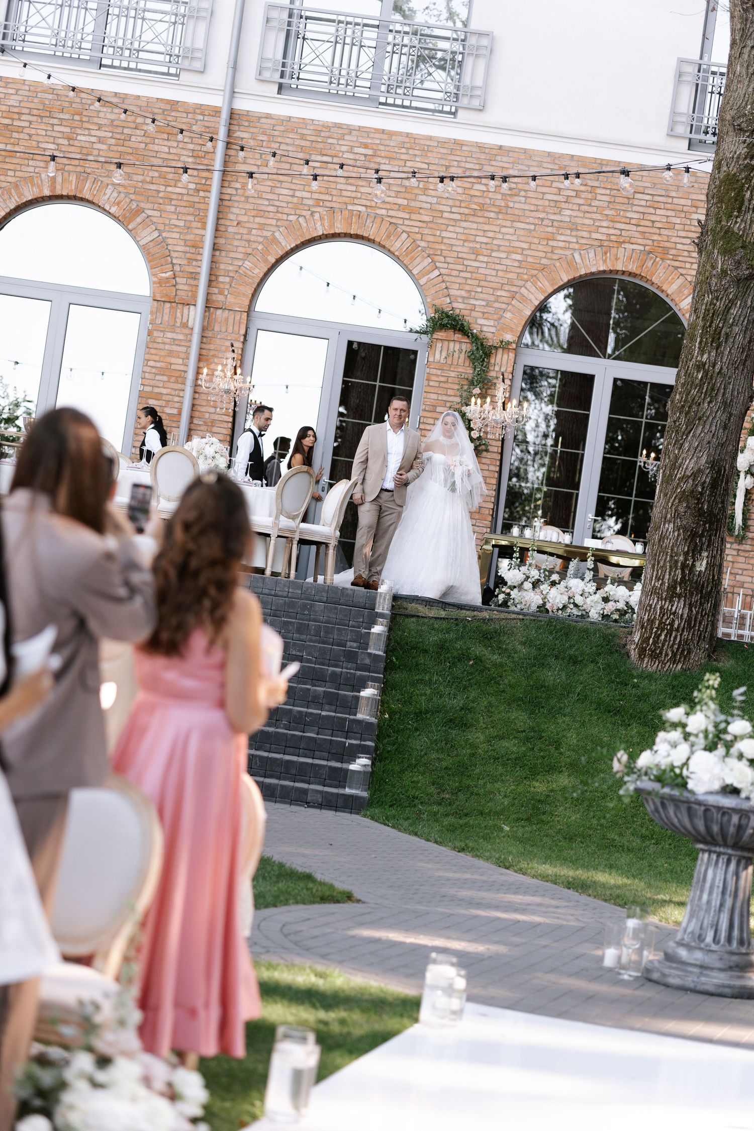 Outdoor wedding venue with brick arches and white floral decorations on steps.