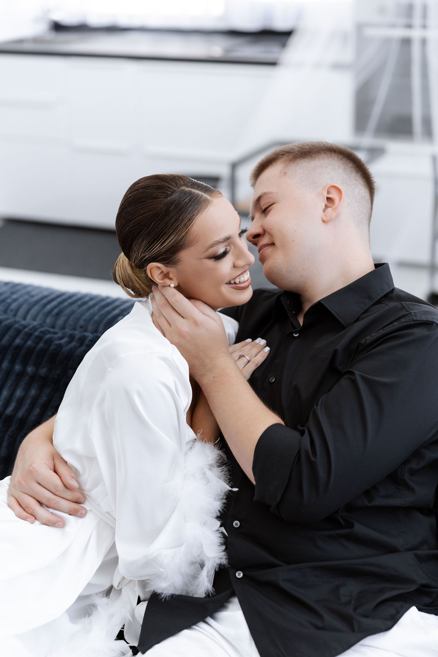 Intimate couple moment on a dark couch in a modern white interior setting.