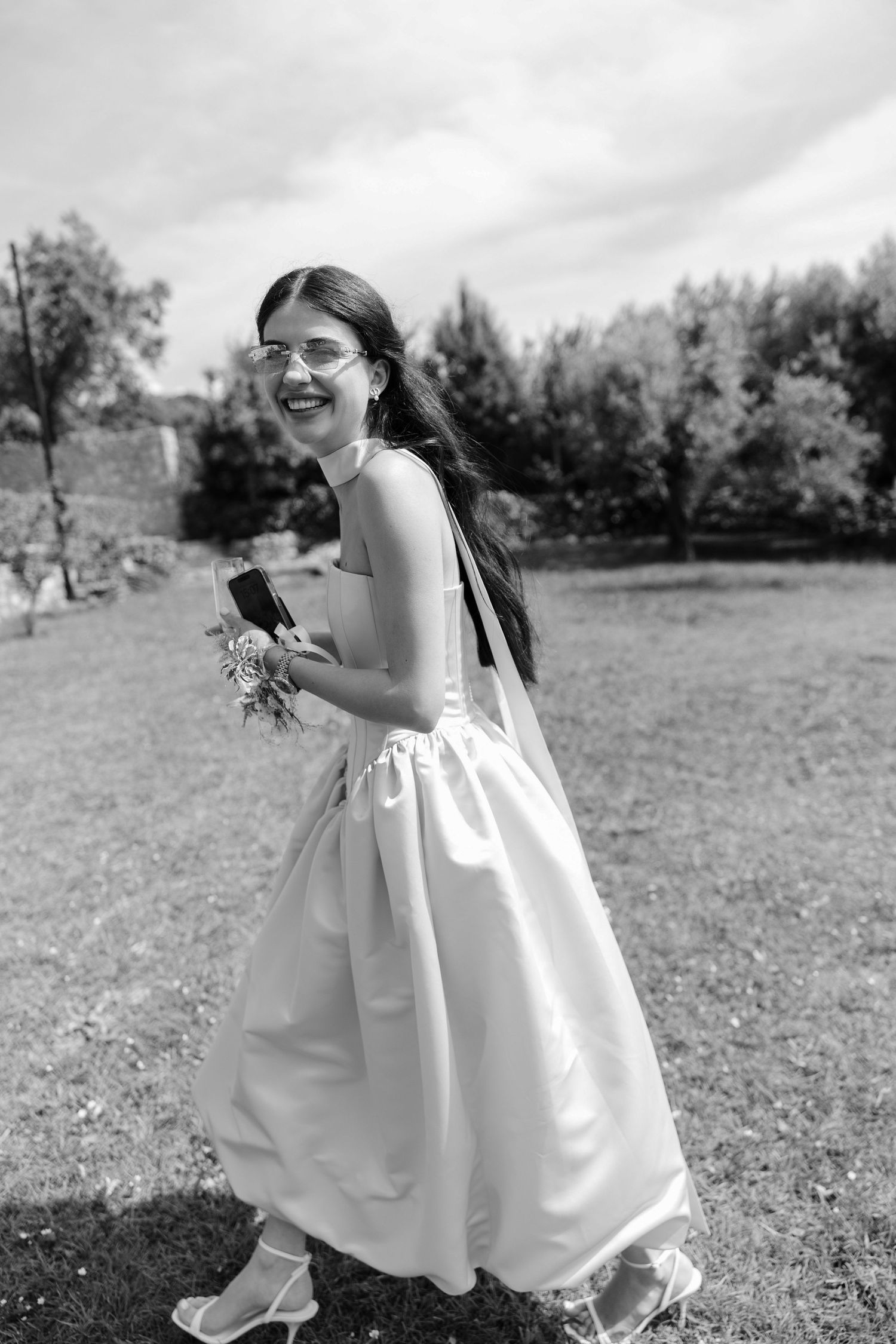 A young child in a white dress runs playfully through a grassy field on a sunny day, captured in black and white.