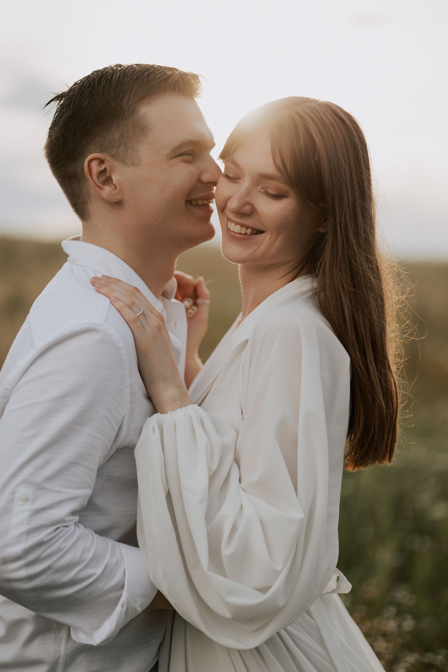 Romantic couple embracing outdoors in white clothing during sunset photoshoot.