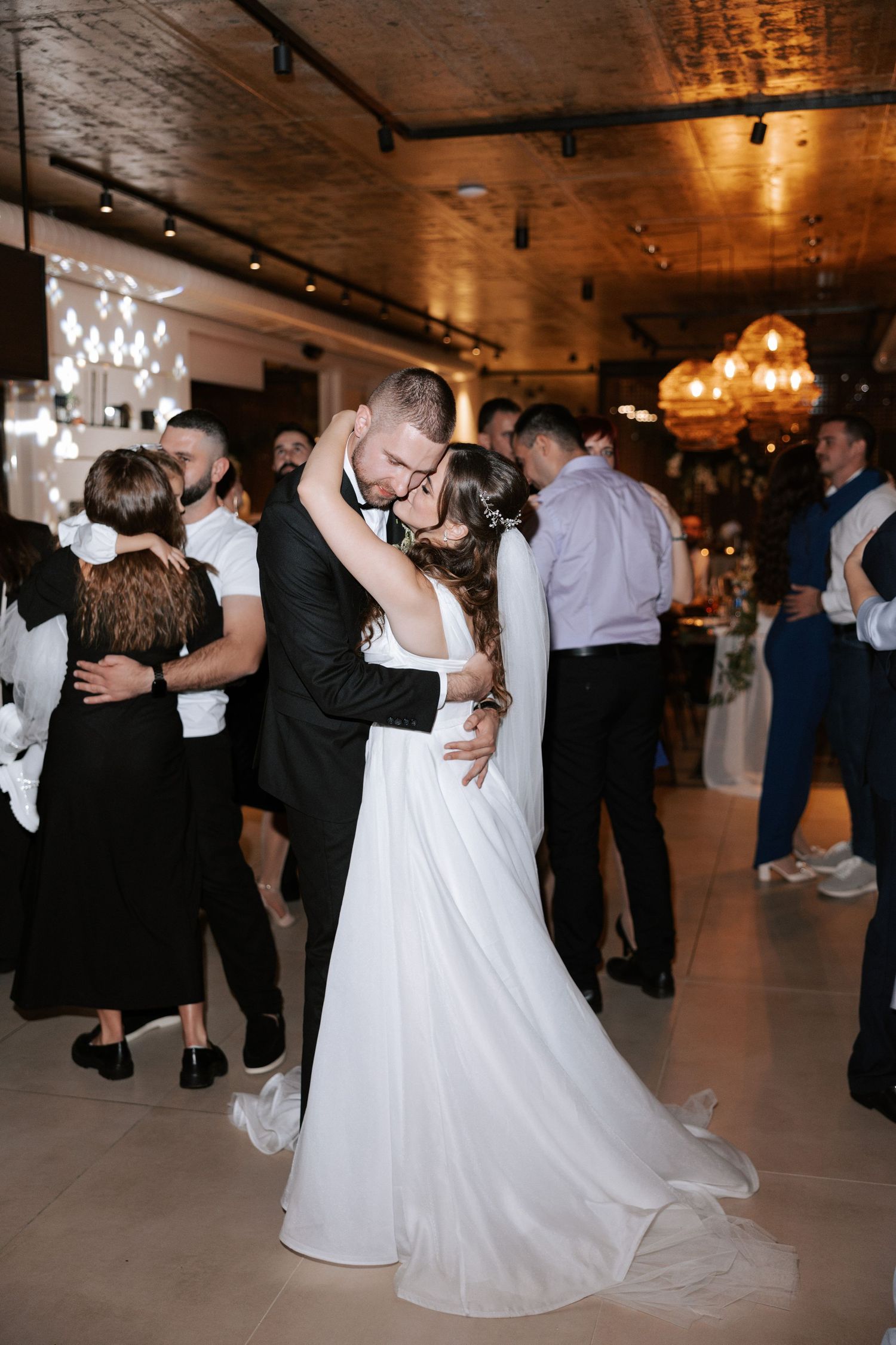 A couple shares their first dance at a wedding reception under warm lighting and crystal chandeliers.