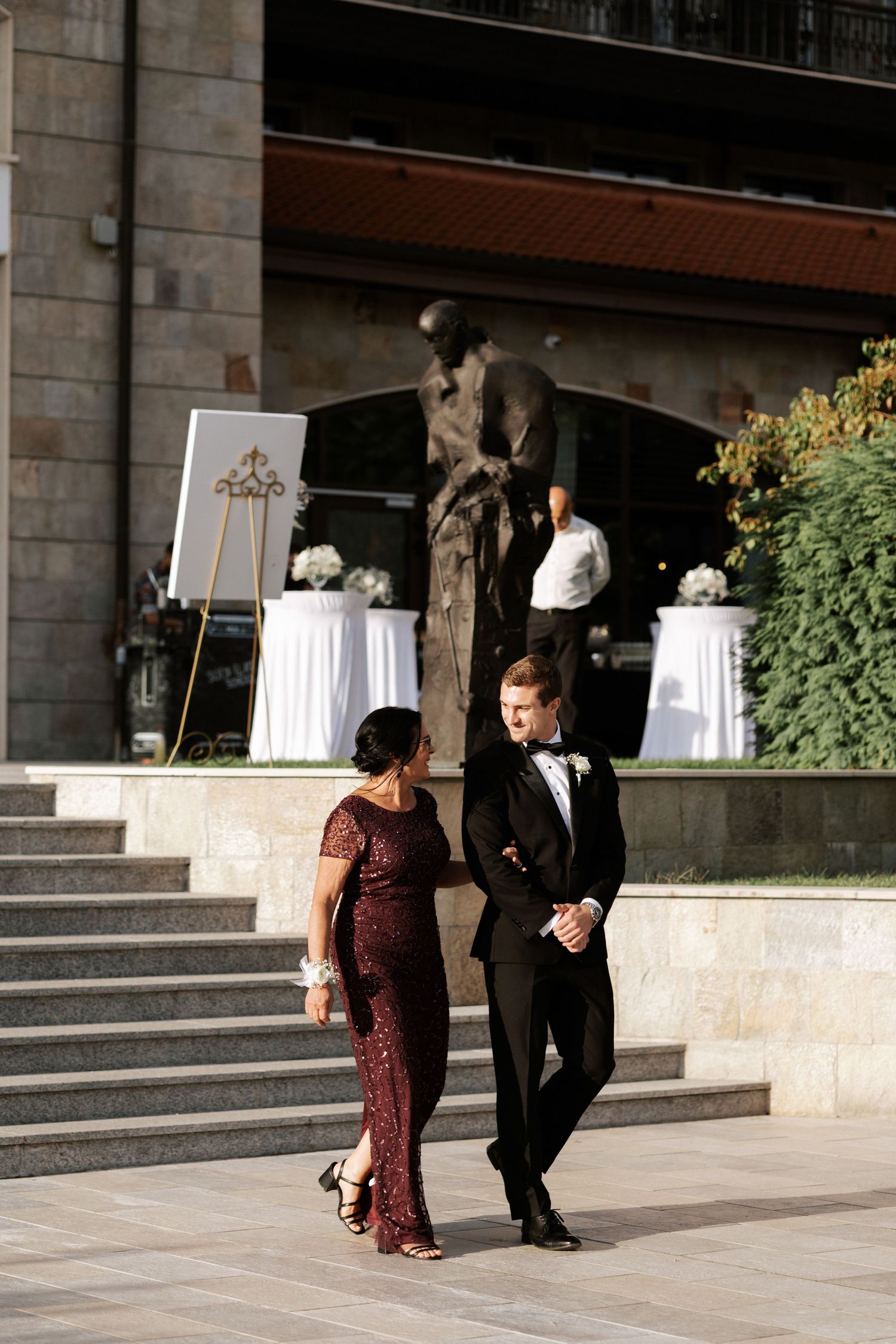Formal event attendees walking up stone stairs at outdoor venue.