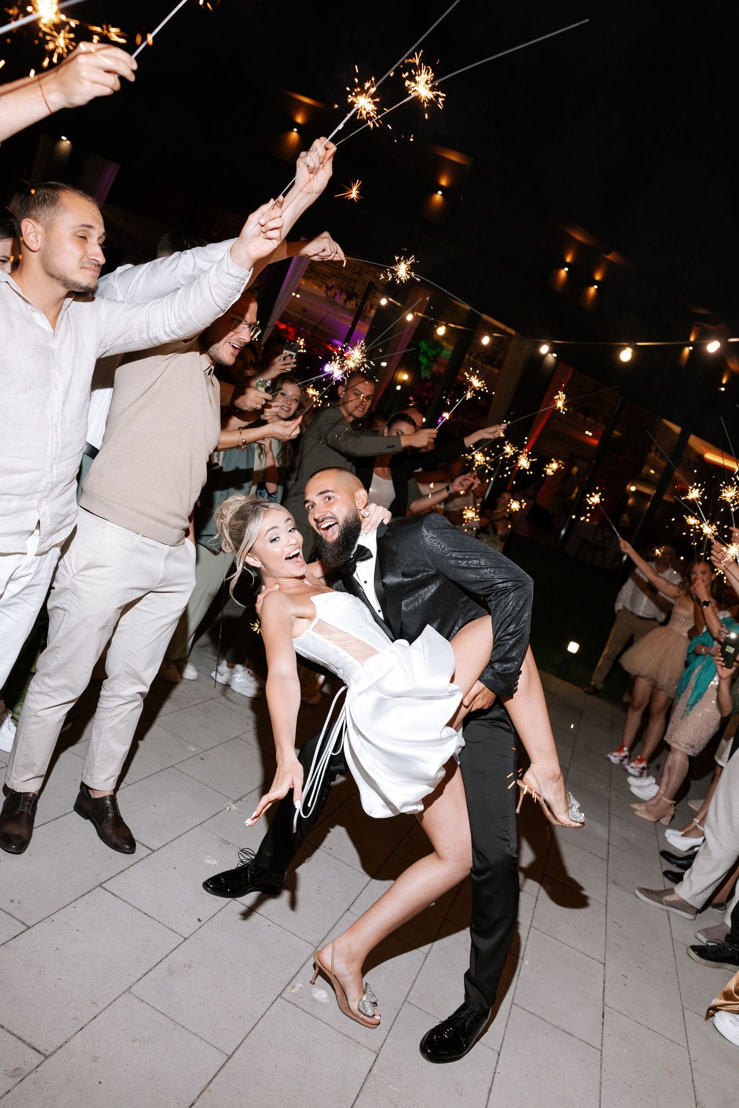 Wedding guests dance and celebrate on a white tiled dance floor at an evening reception party.