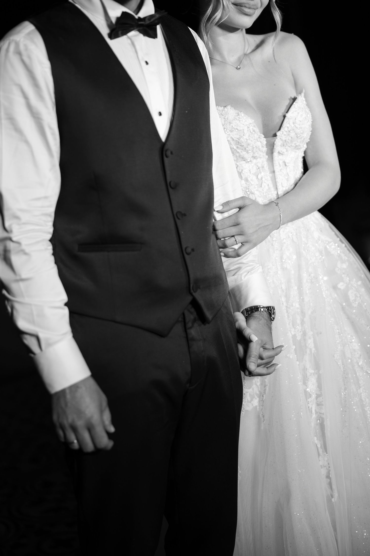 Black and white wedding photo series showing close-up details of bride in lace dress with groom in formal vest and tie.