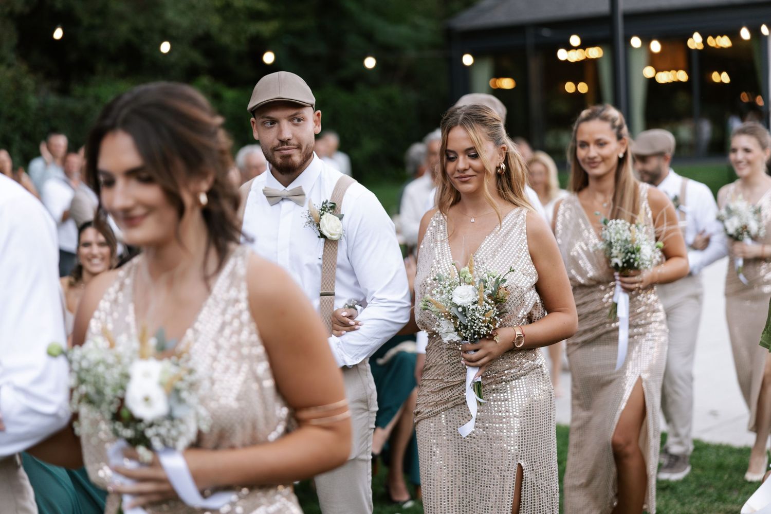 Wedding guests dance and celebrate at an outdoor evening reception under string lights and trees.