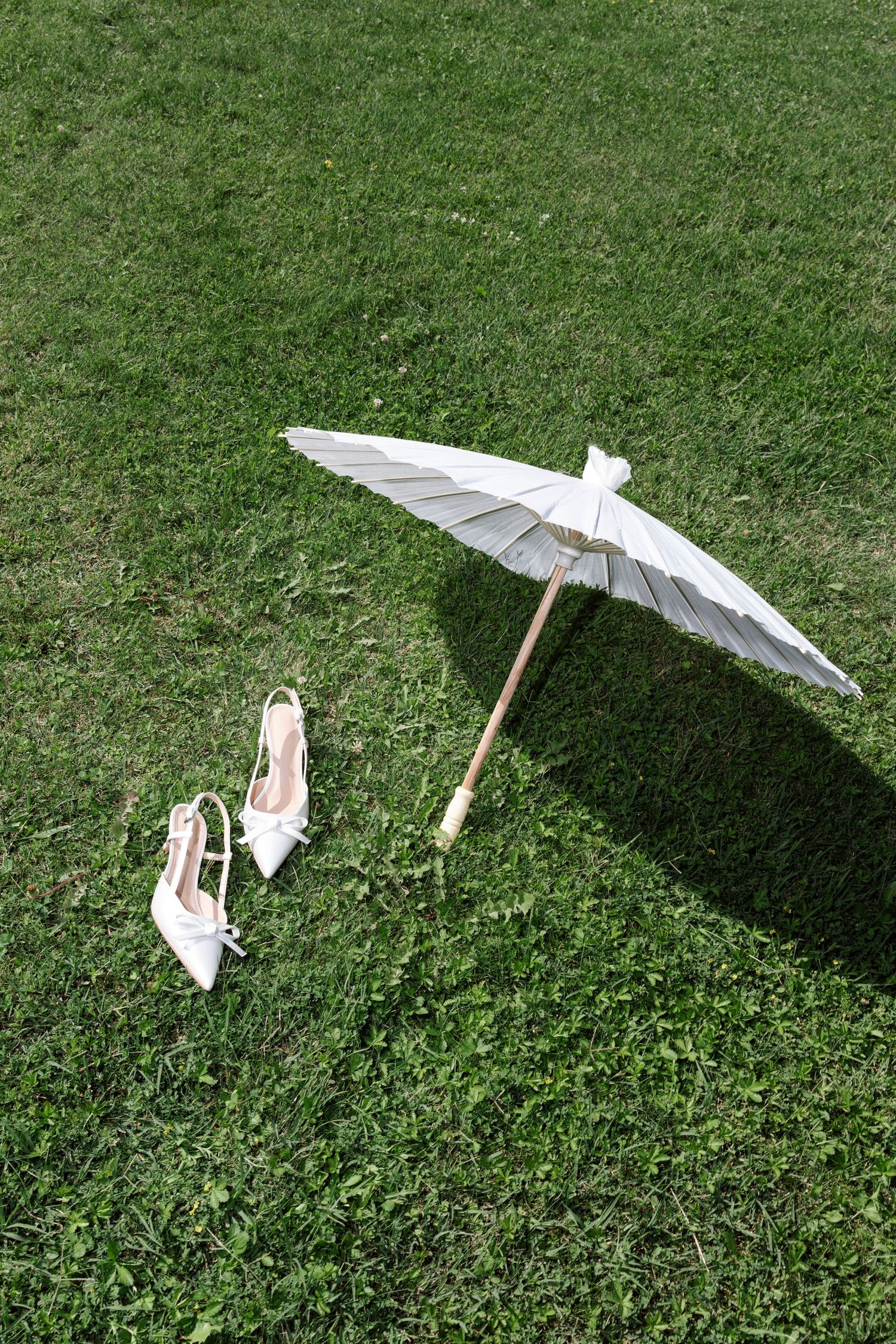 Small white decorative paper parasol laying on green grass casting a shadow in sunlight.