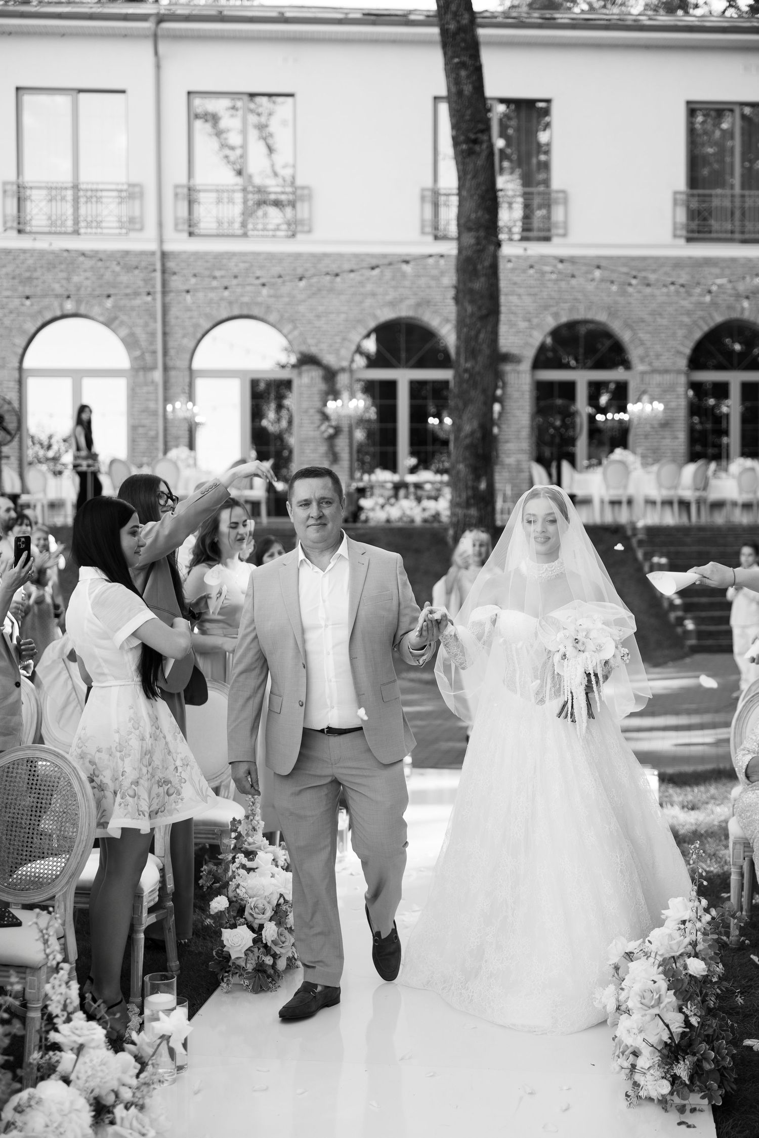 Black and white outdoor wedding reception with guests mingling around floral decorations.