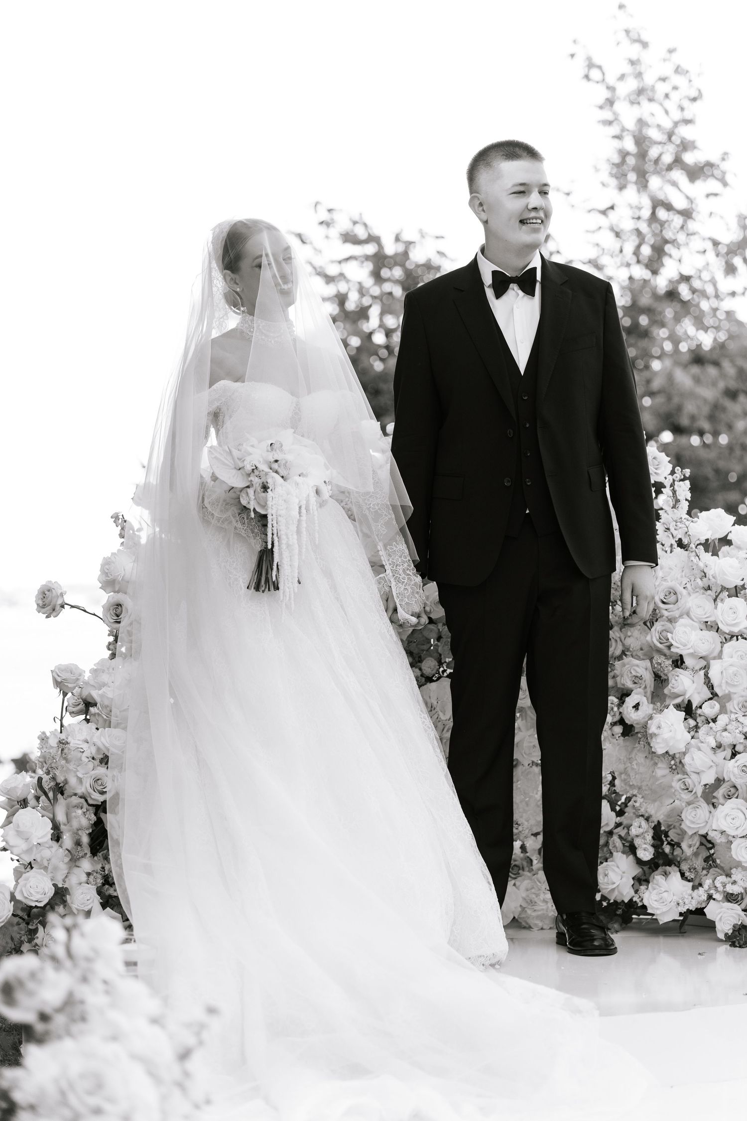 A wedding couple poses against a backdrop of white floral arrangements in an elegant black and white setting.
