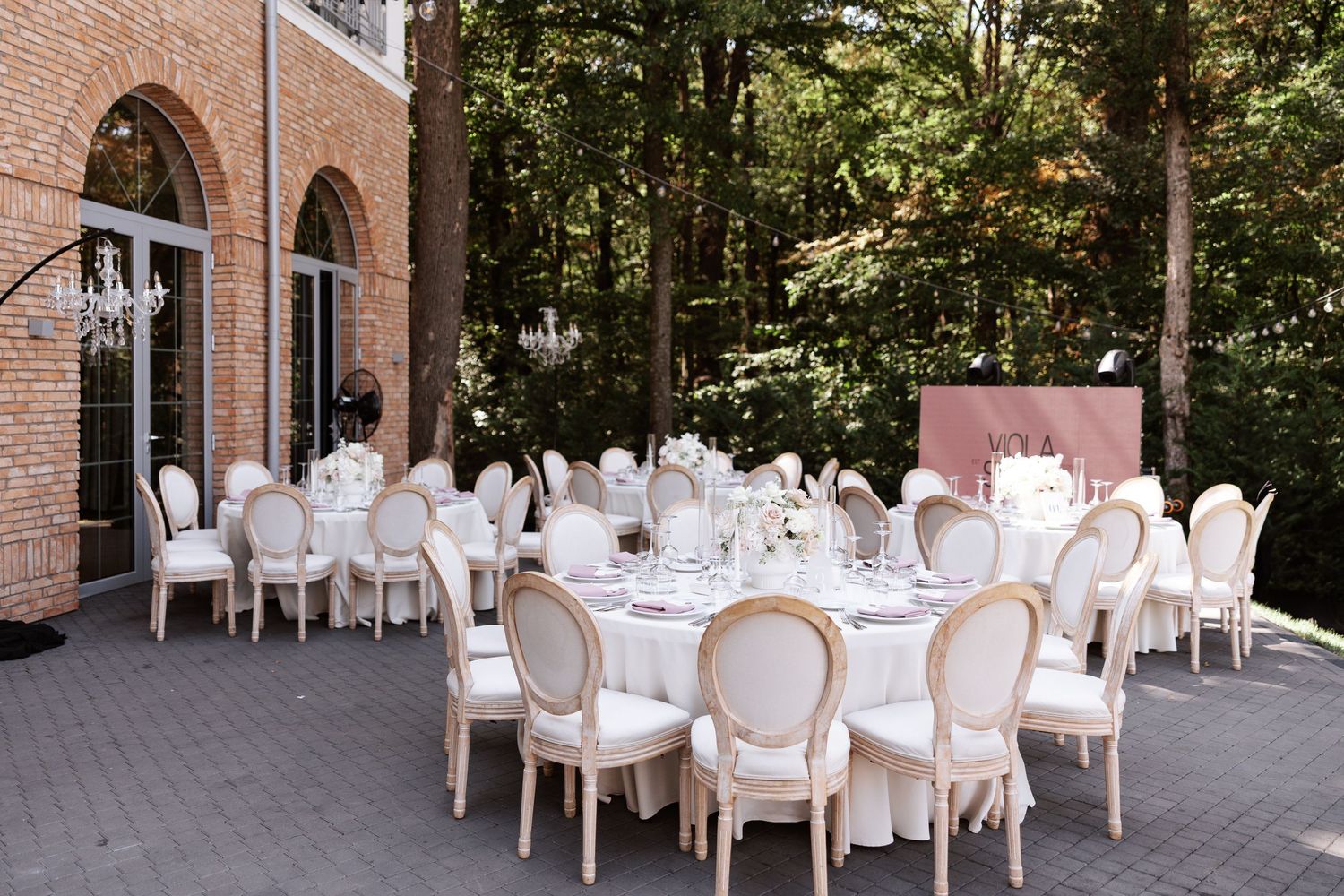 Elegant wedding reception setup with white chairs and tables in a brick courtyard.