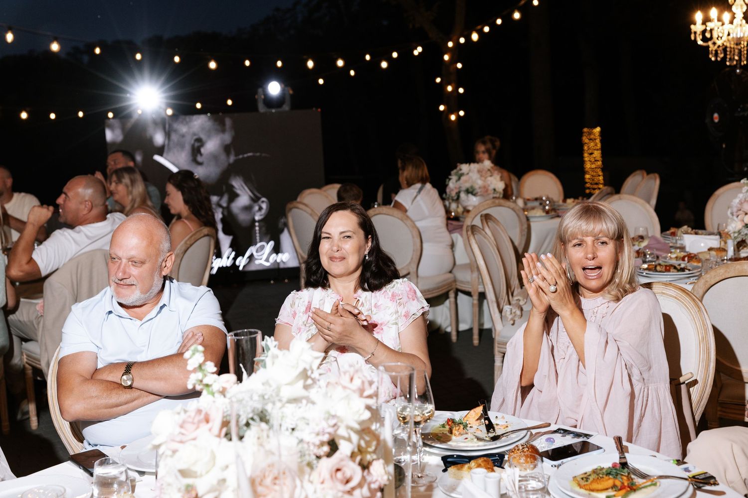 Wedding reception dinner under string lights with elegant table settings.