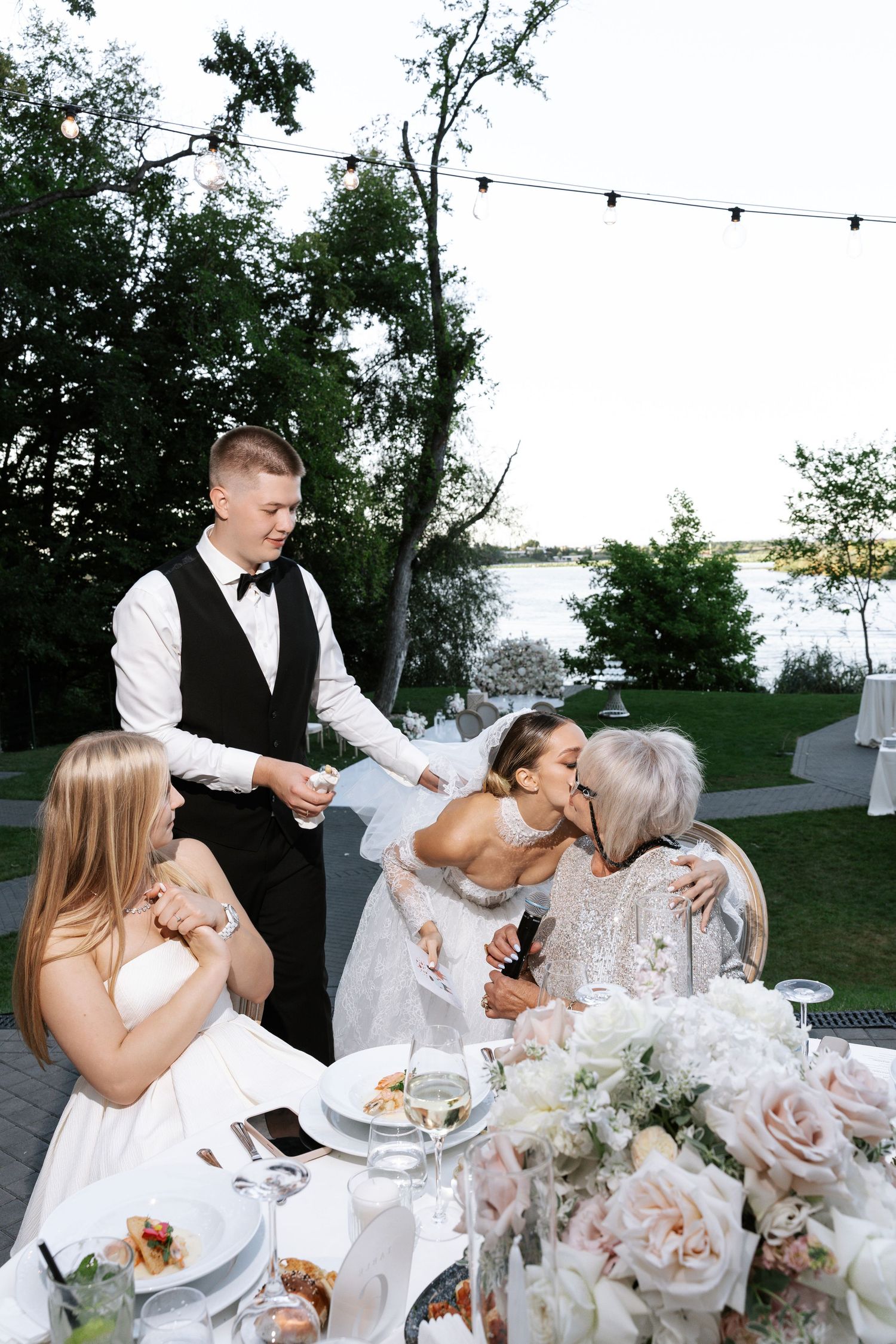 Wedding guests enjoying cake and refreshments at an outdoor reception with string lights.