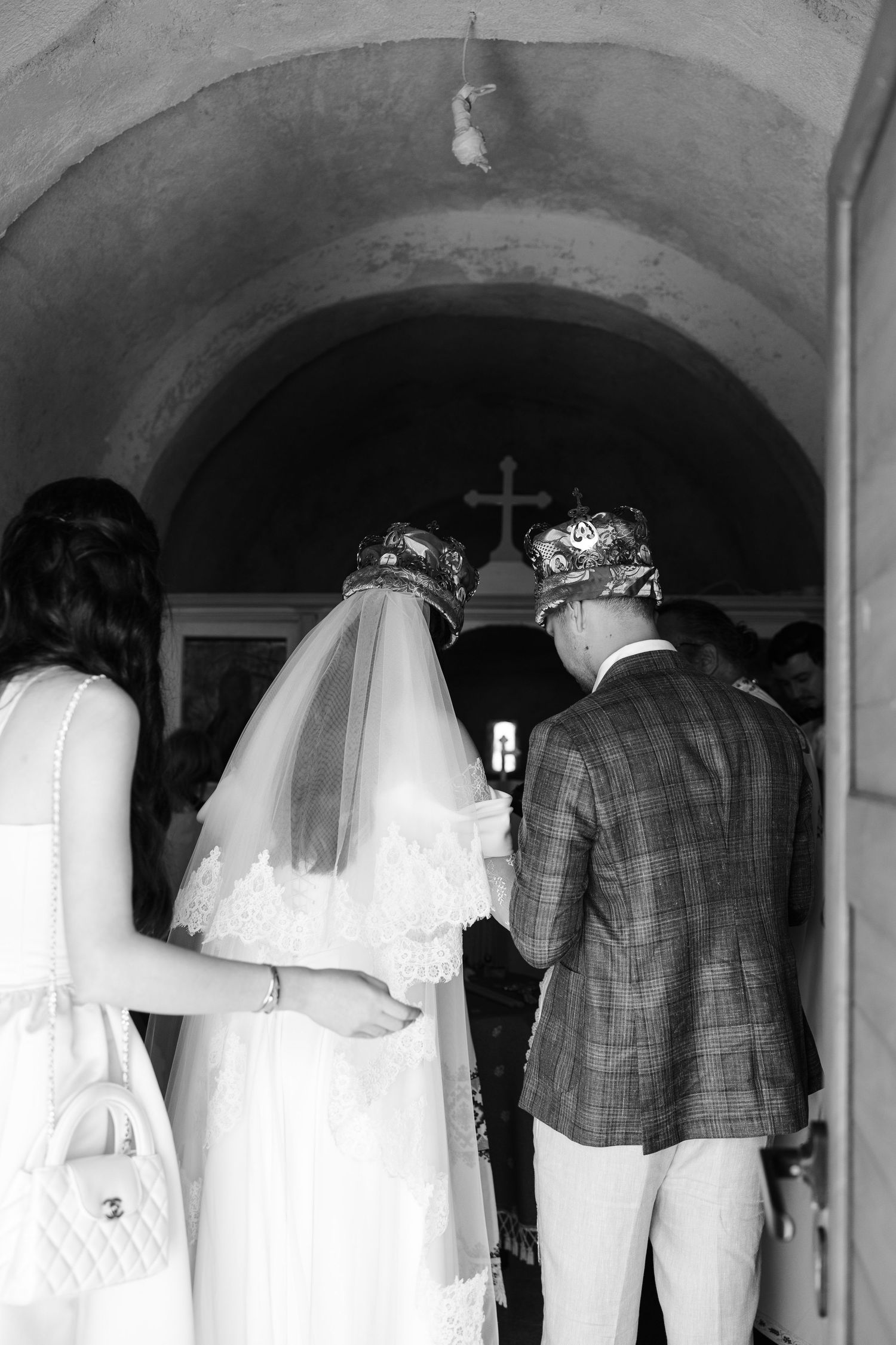 A black and white photo shows a line of people with white veils looking at a wall in an arched hallway.
