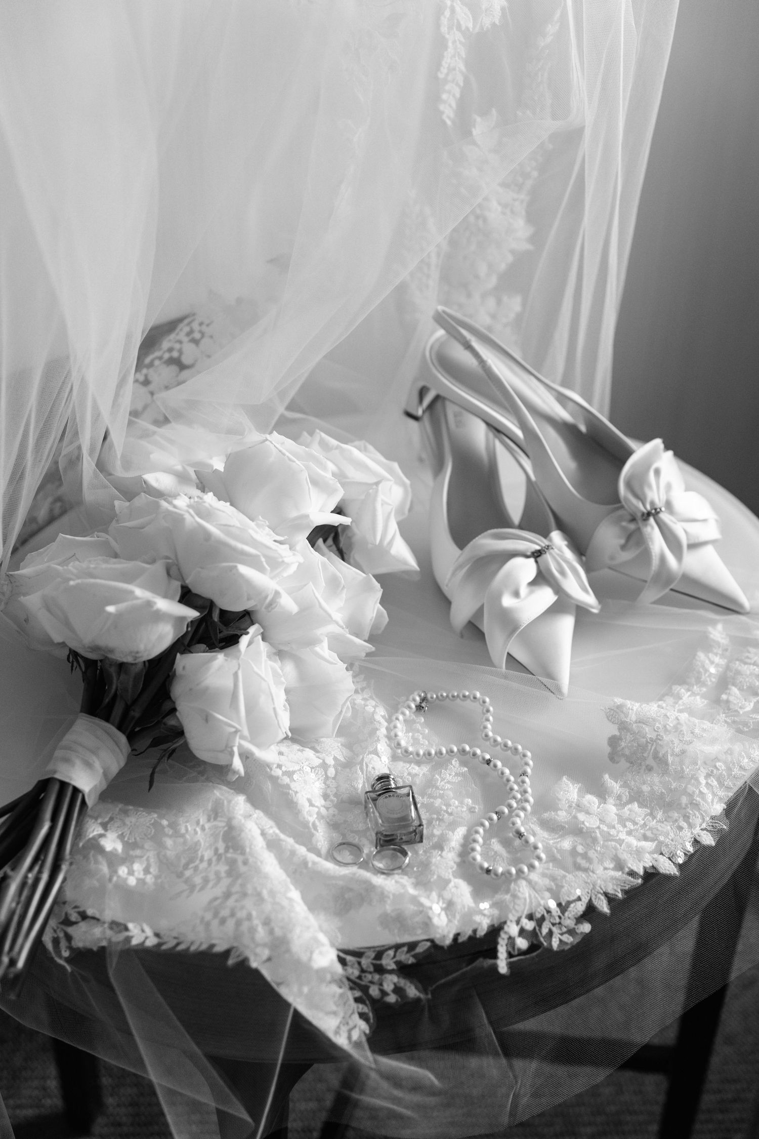 Artistic black and white close-up of delicate white bridal veil with lace trim and pearl details arranged in sequence.