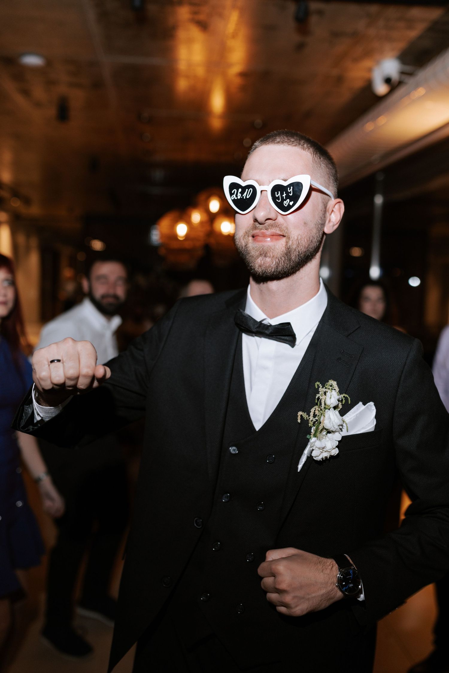 A wedding guest dancing while wearing heart-shaped sunglasses and a black tuxedo.