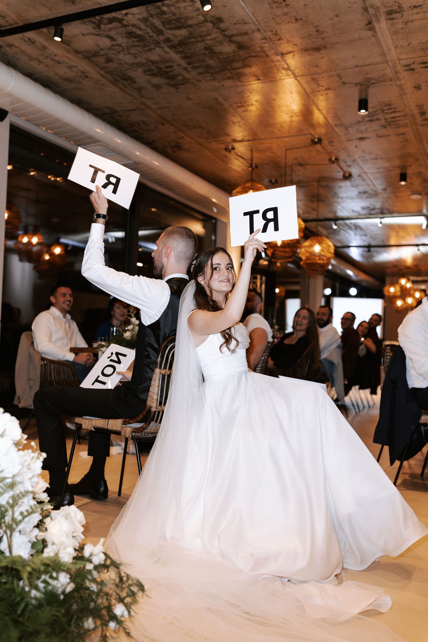 Wedding couple holding up RT signs during a reception in an industrial-style venue with exposed ceiling.