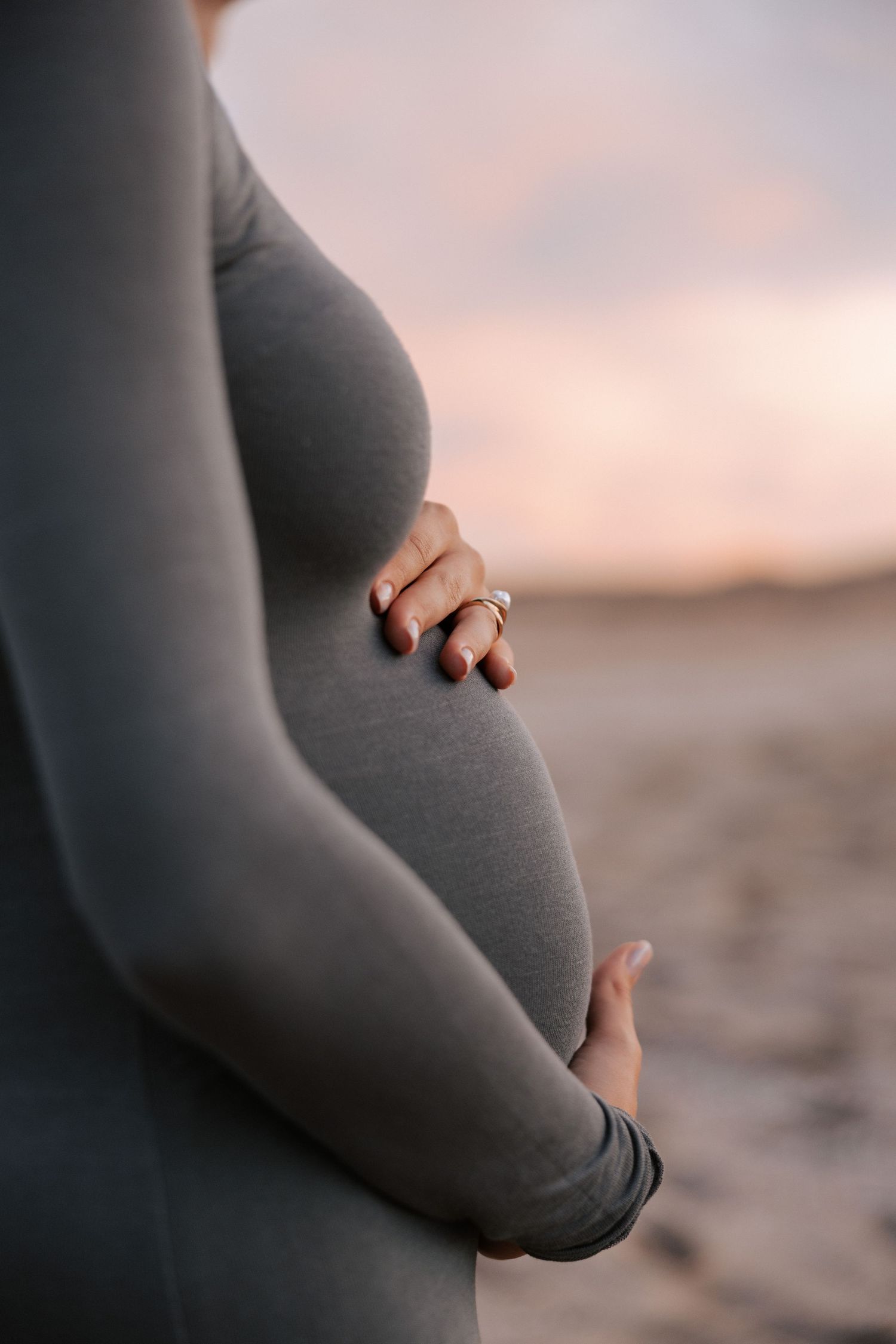 Close-up maternity photo showing pregnant belly with wedding ring visible at sunset.