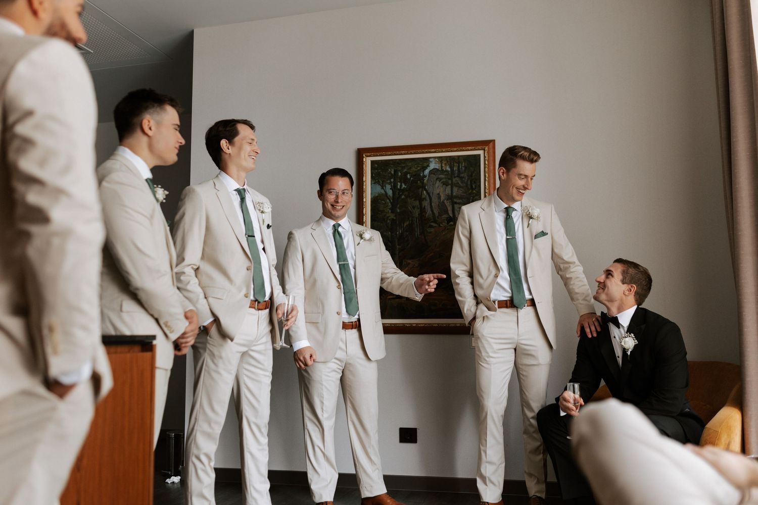 Wedding party in white suits gather around someone in black tuxedo in indoor setting.