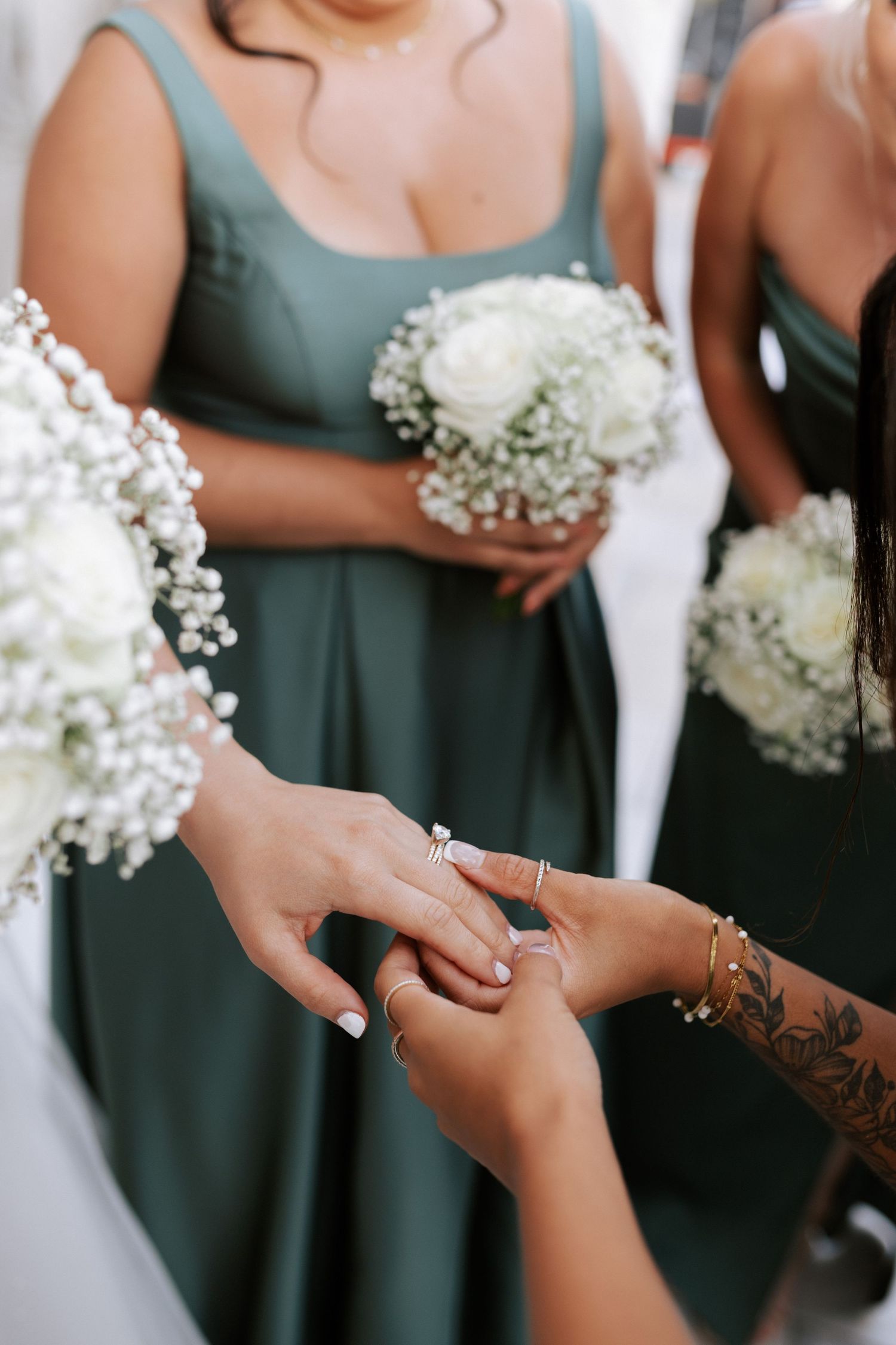 Close-up of hands holding white baby's breath bouquets with rings and tattoo detail.