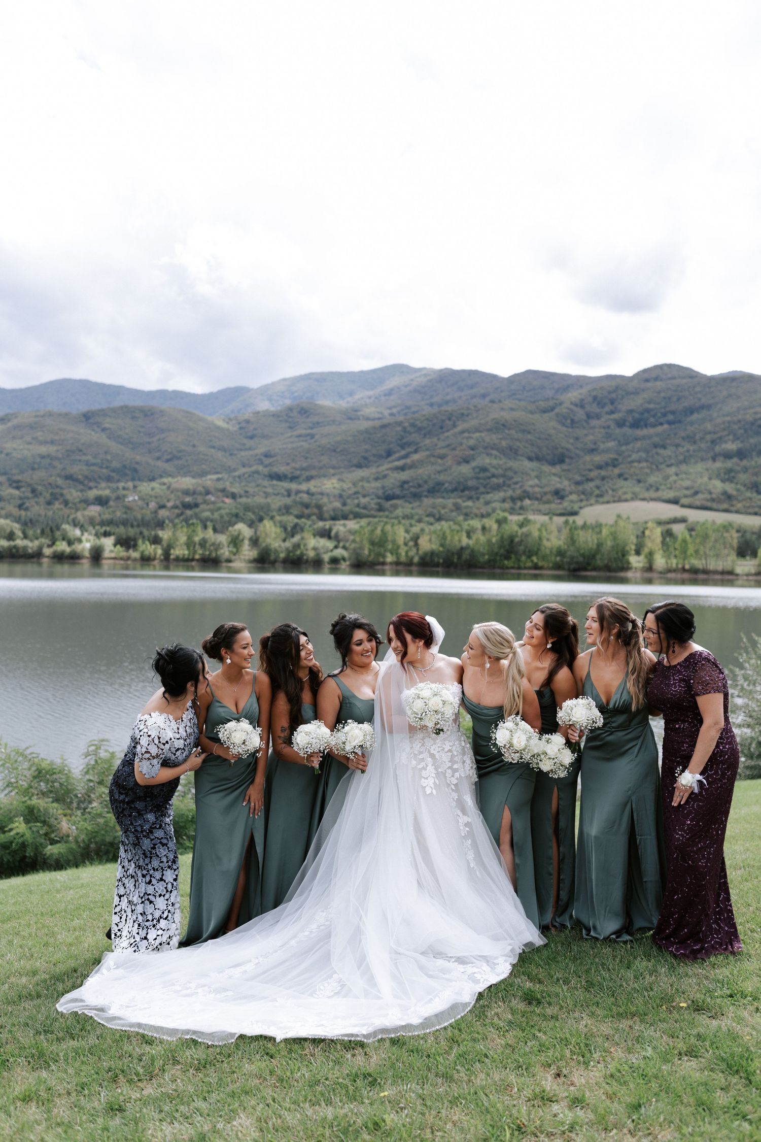 Wedding party in green dresses and formal attire gathered by a scenic mountain lake.
