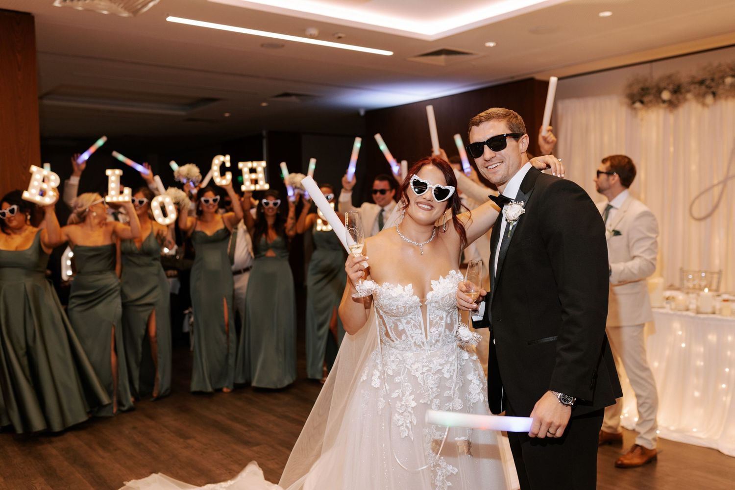 Wedding party celebration with light-up foam sticks in elegant reception venue.