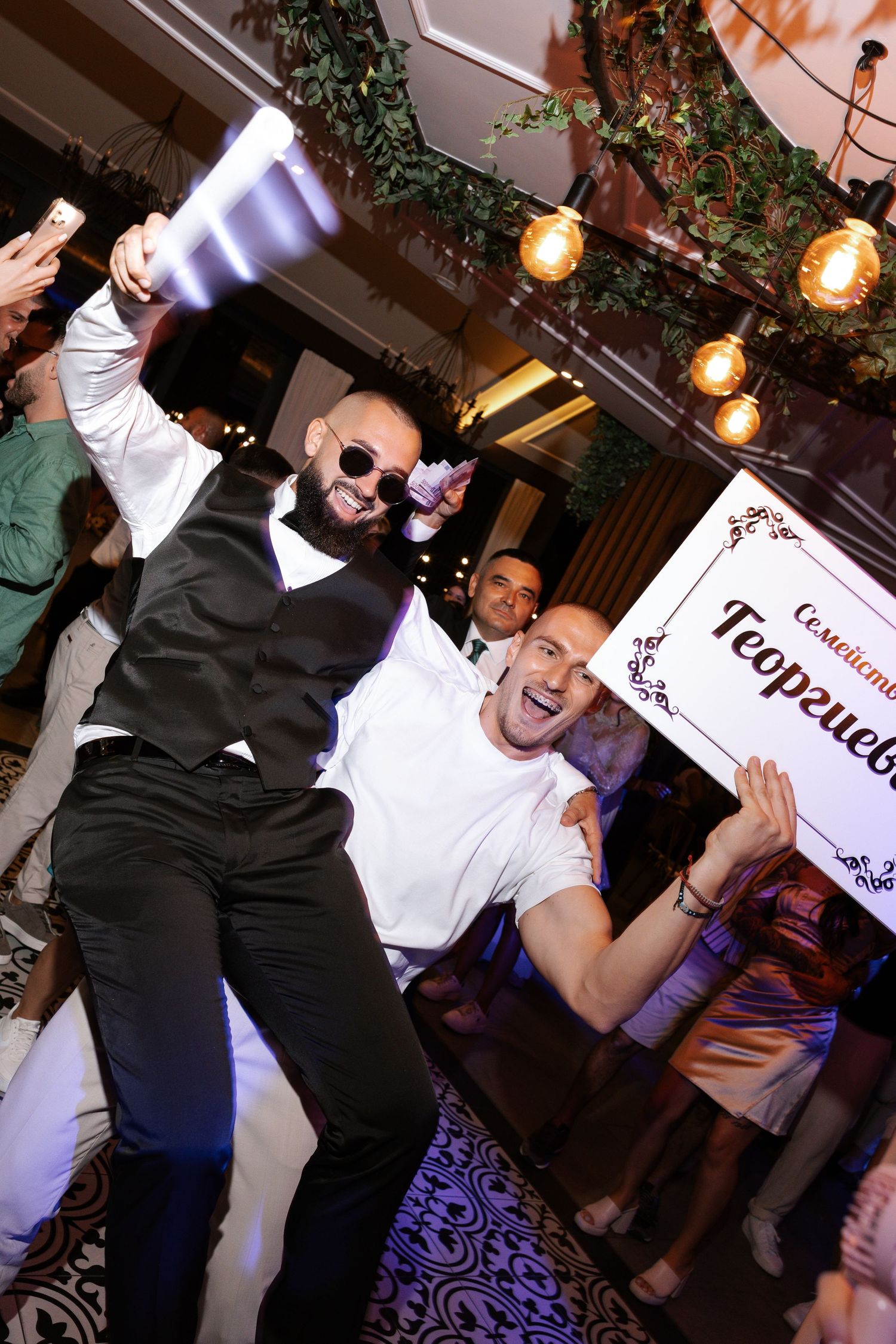 People dancing and having fun at a party with hanging lights and decorative elements in the background.