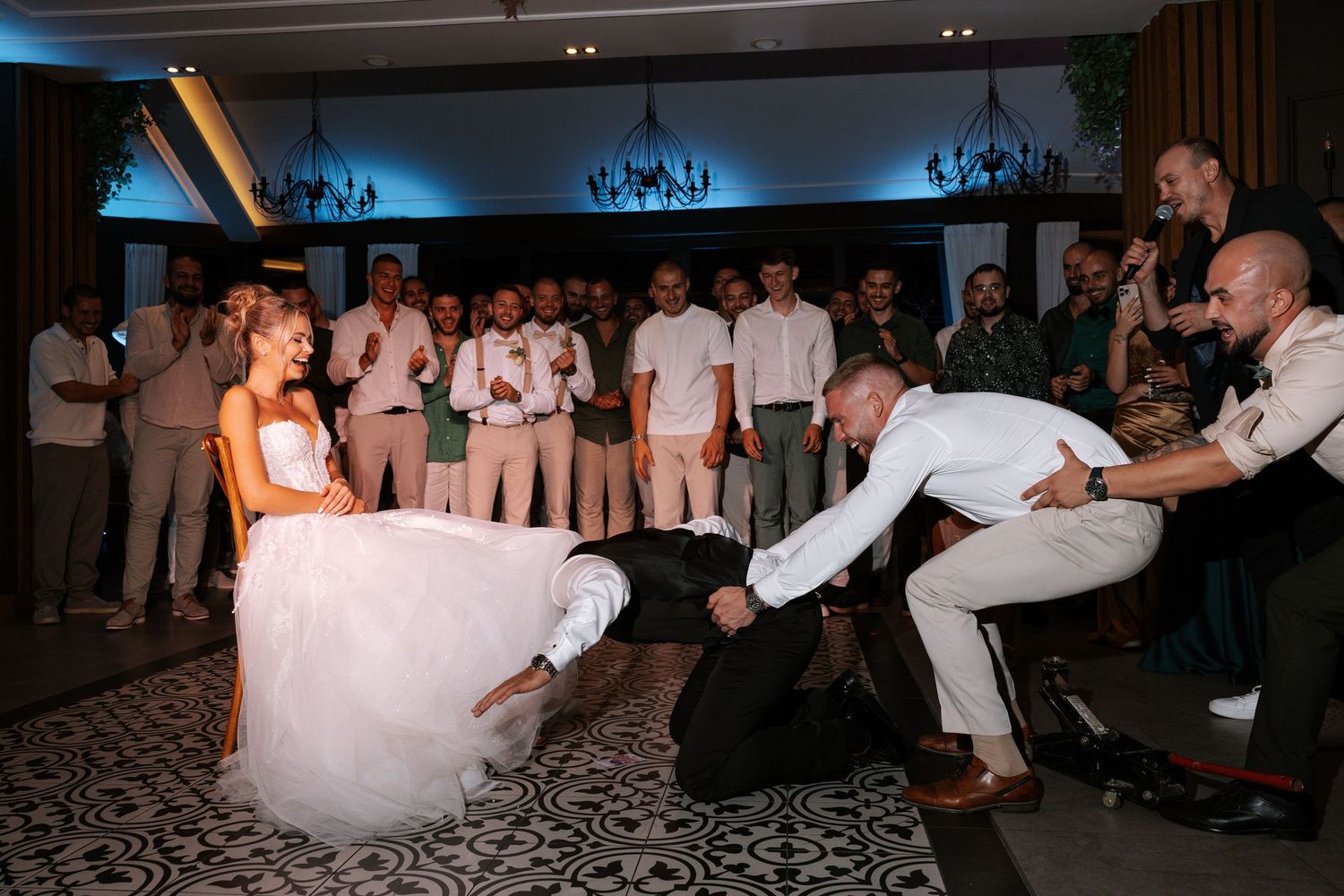 Wedding guests gather around a dance floor as a bride in a white gown participates in a fun reception dance moment.