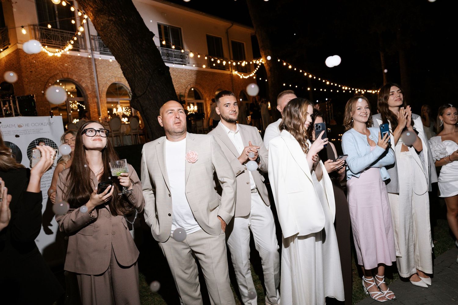 Wedding guests dancing and celebrating at a nighttime reception with string lights.