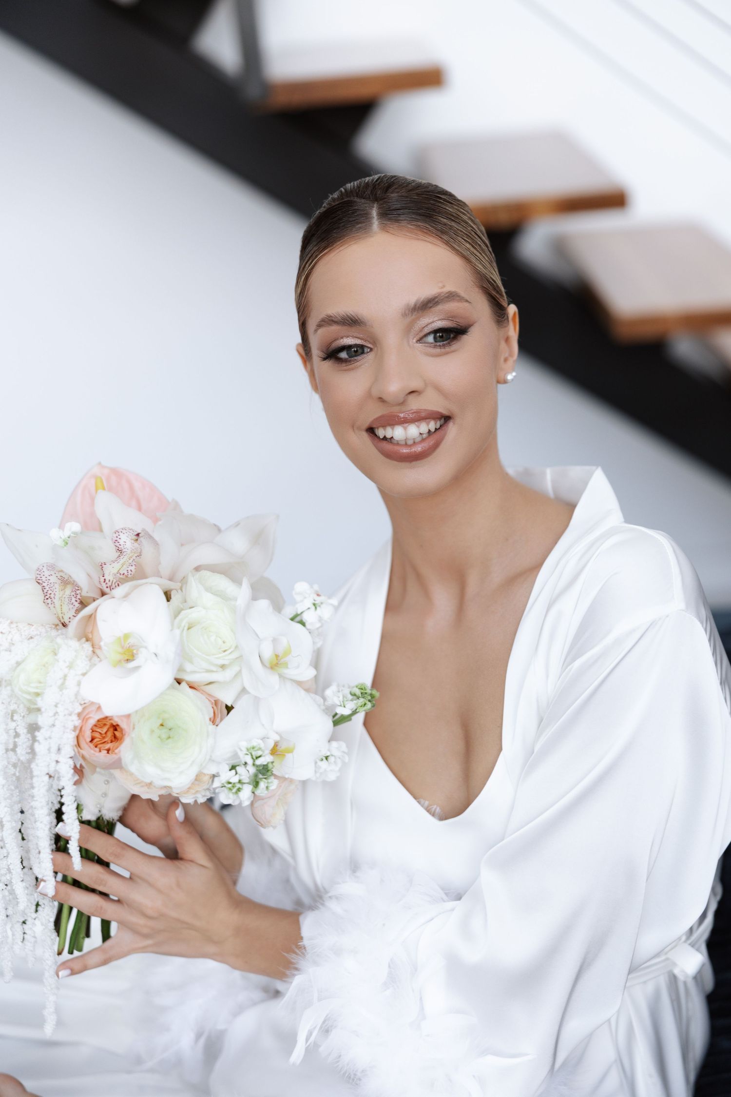A delicate bridal bouquet featuring peach and white flowers held by someone wearing a white robe.