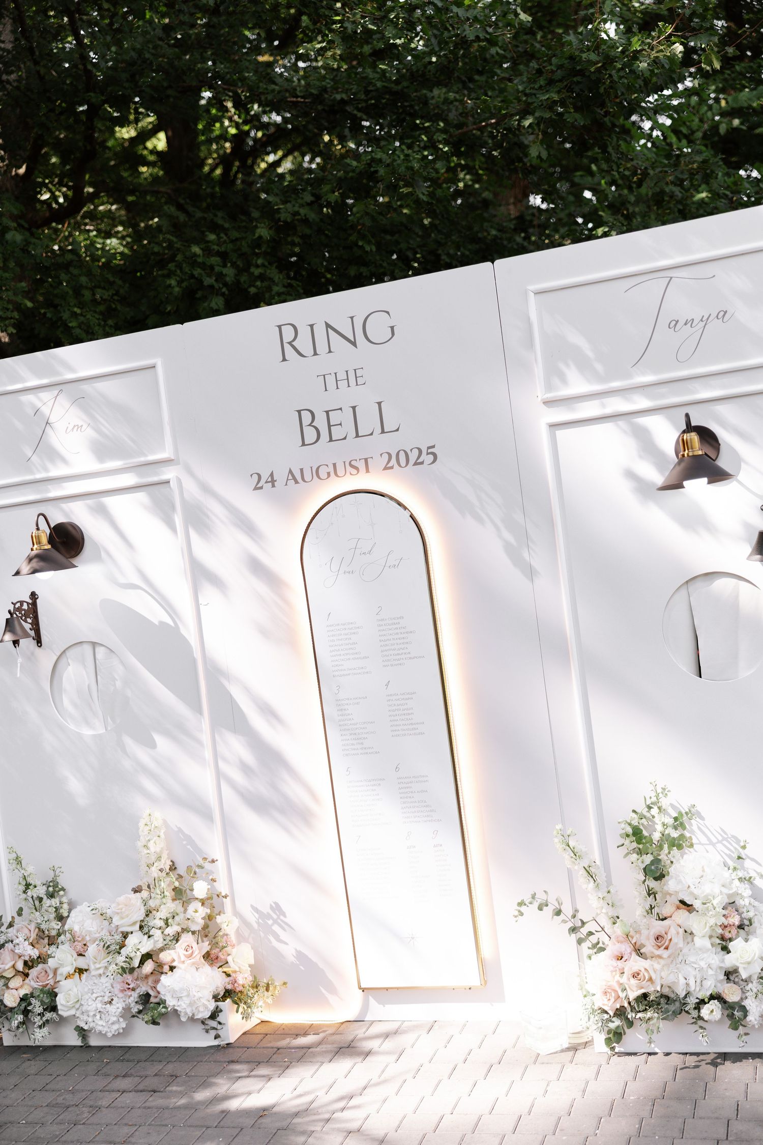 An elegant white wedding backdrop with floral arrangements and illuminated text displays.