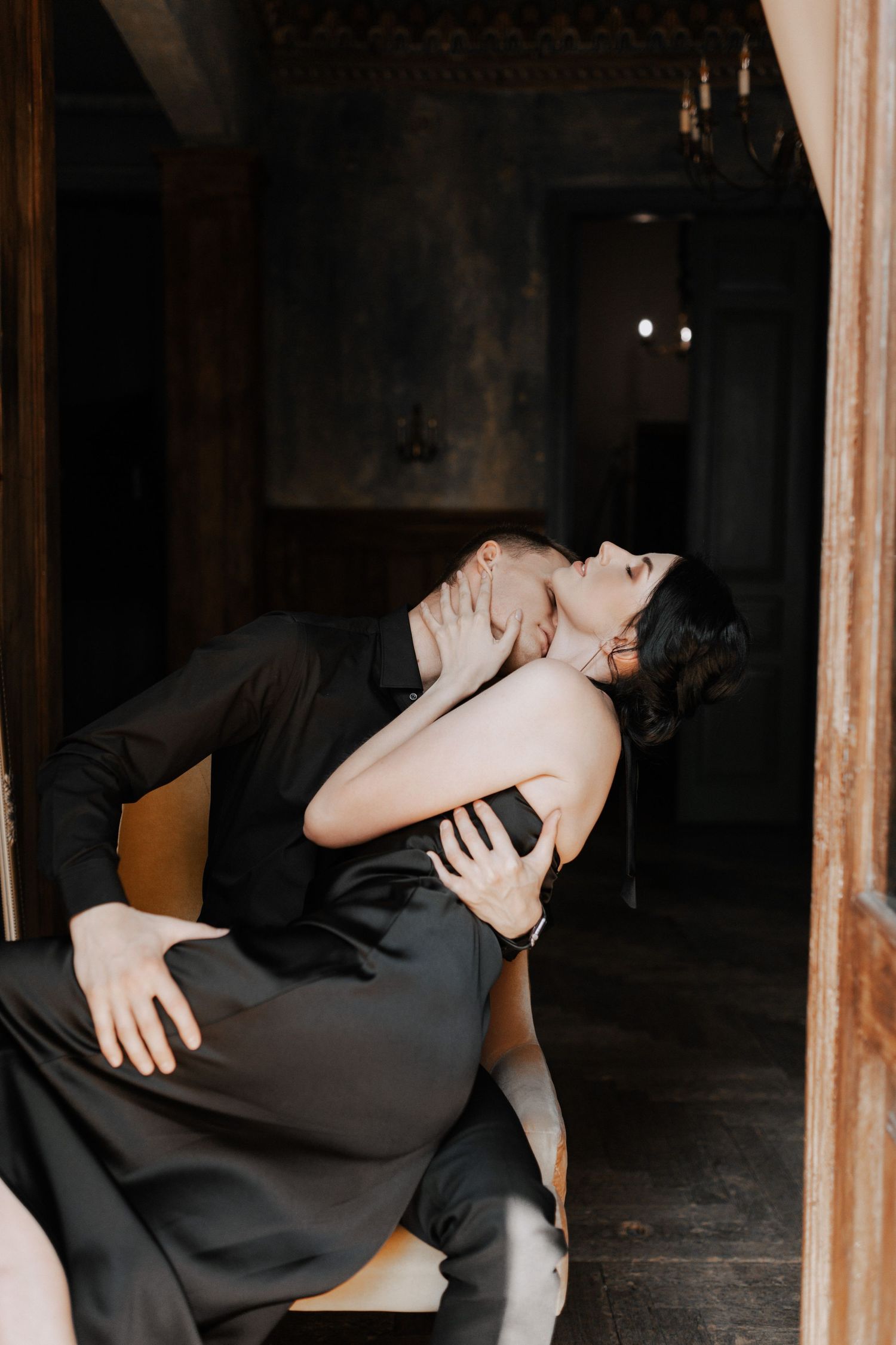Dramatic pose of couple in dark formal attire against vintage doorframe.
