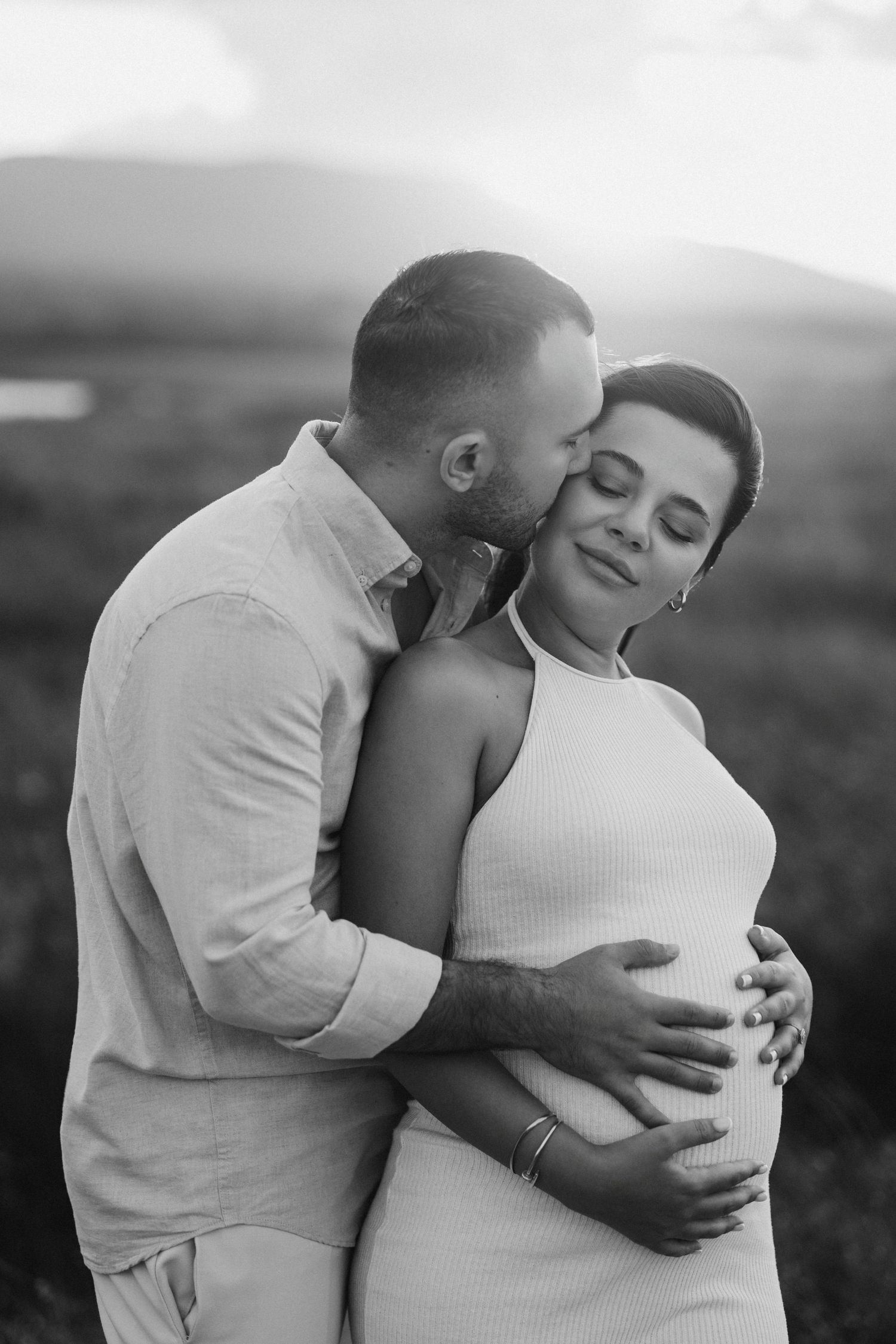 A tender maternity photoshoot of a couple embracing against a misty outdoor backdrop.