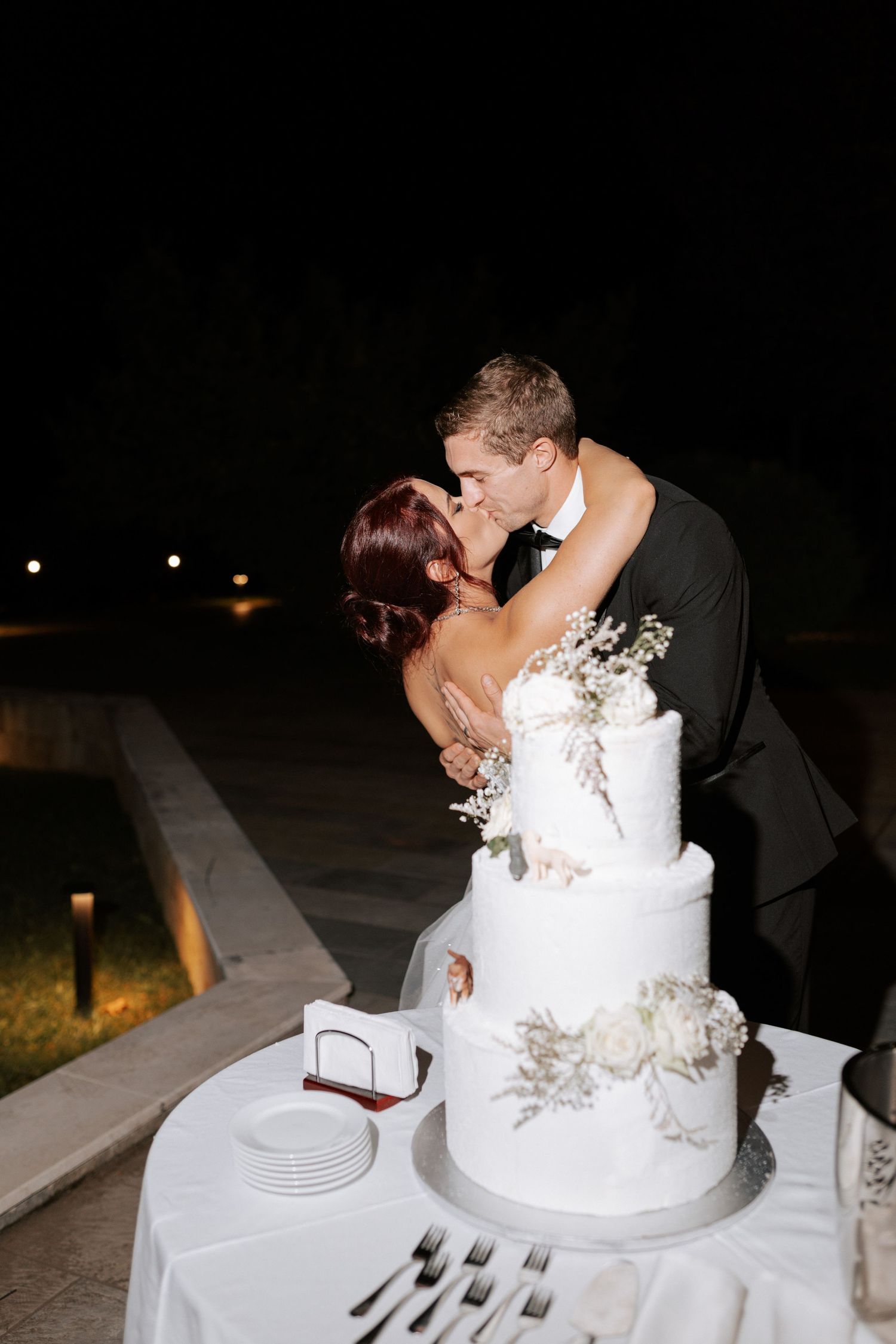 Intimate moment between newlyweds embracing behind their three-tiered white wedding cake.