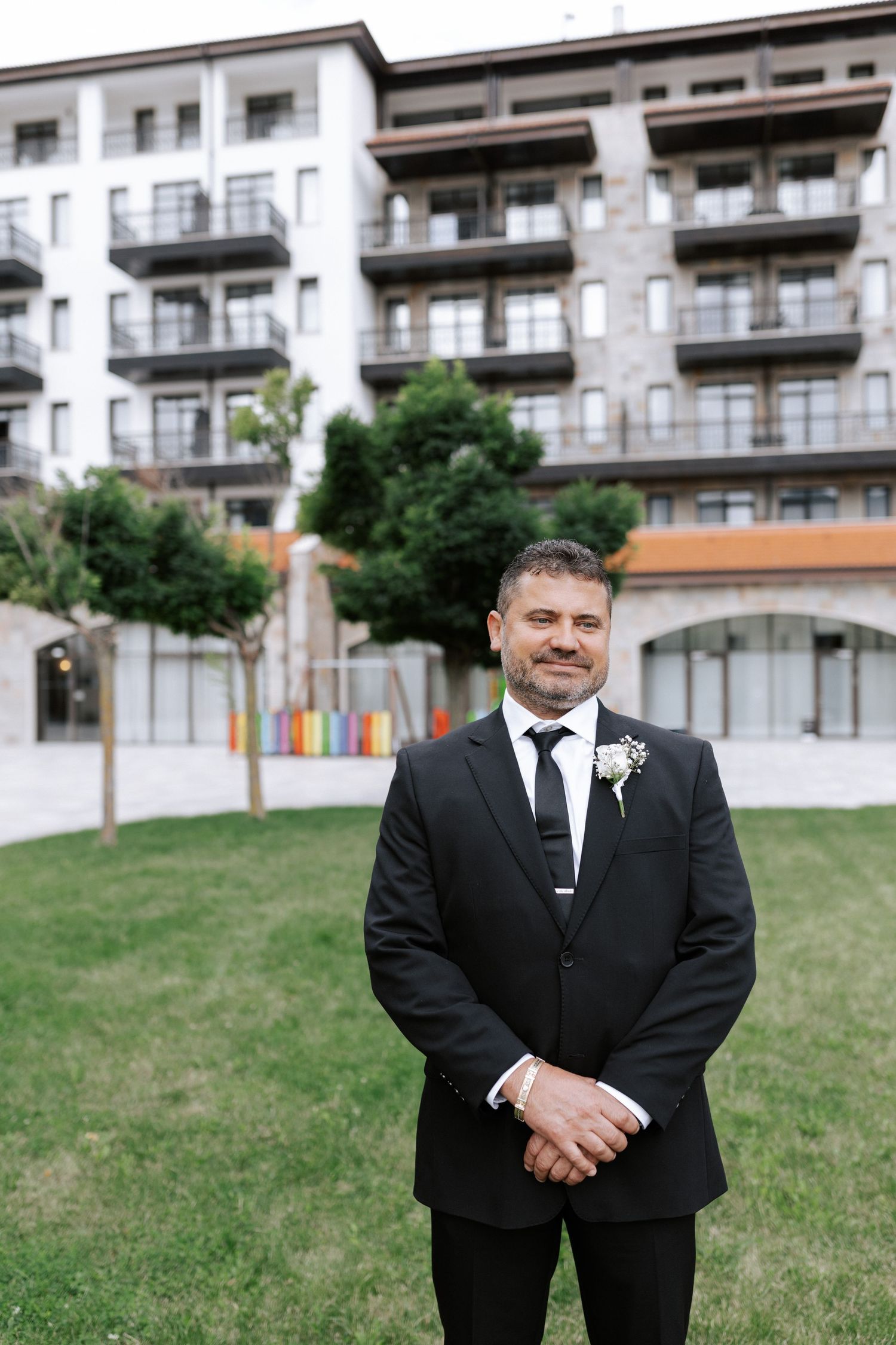 A formal portrait in front of modern apartment building with white and brown exterior.