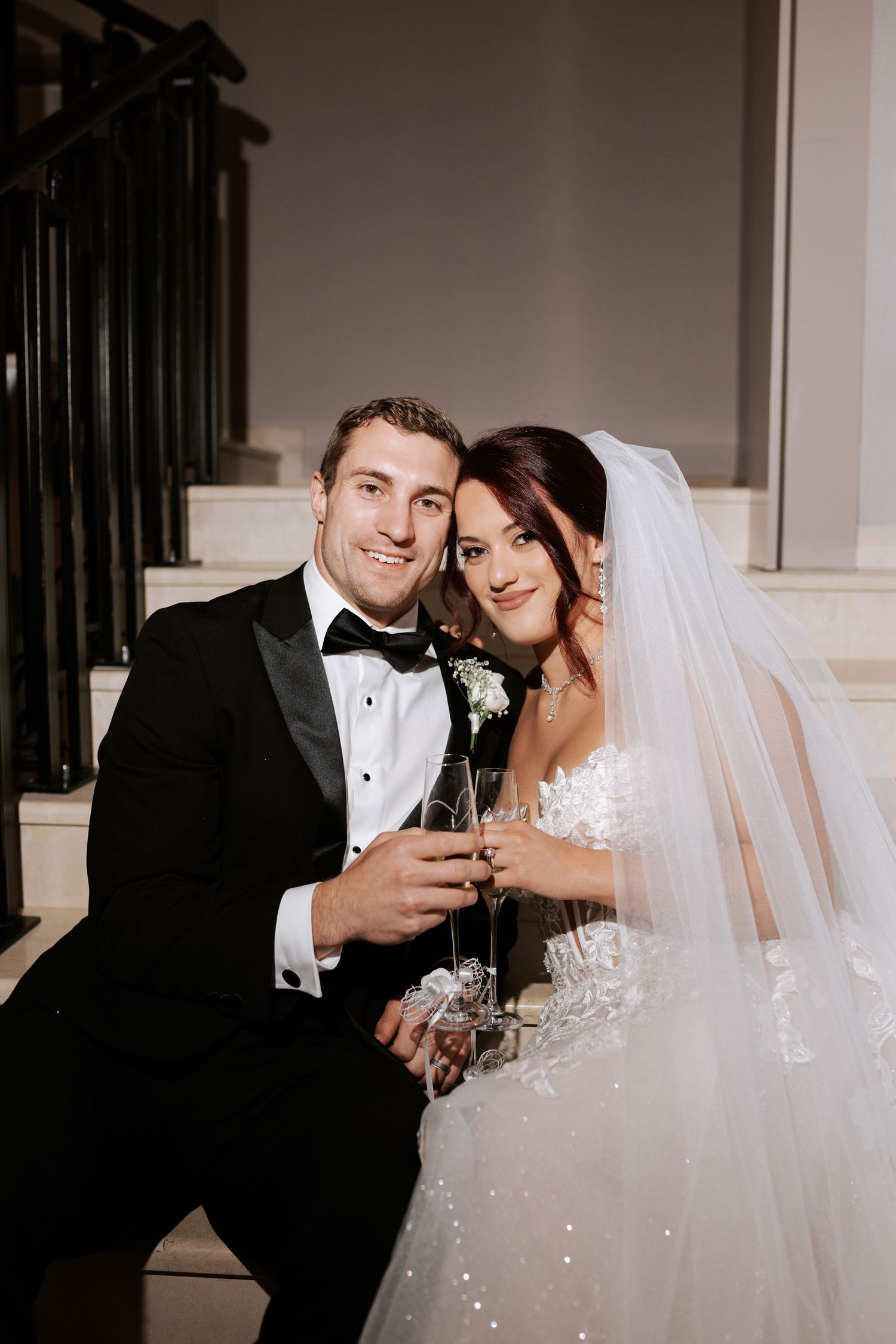 Wedding couple sharing intimate moment on staircase with champagne glasses.