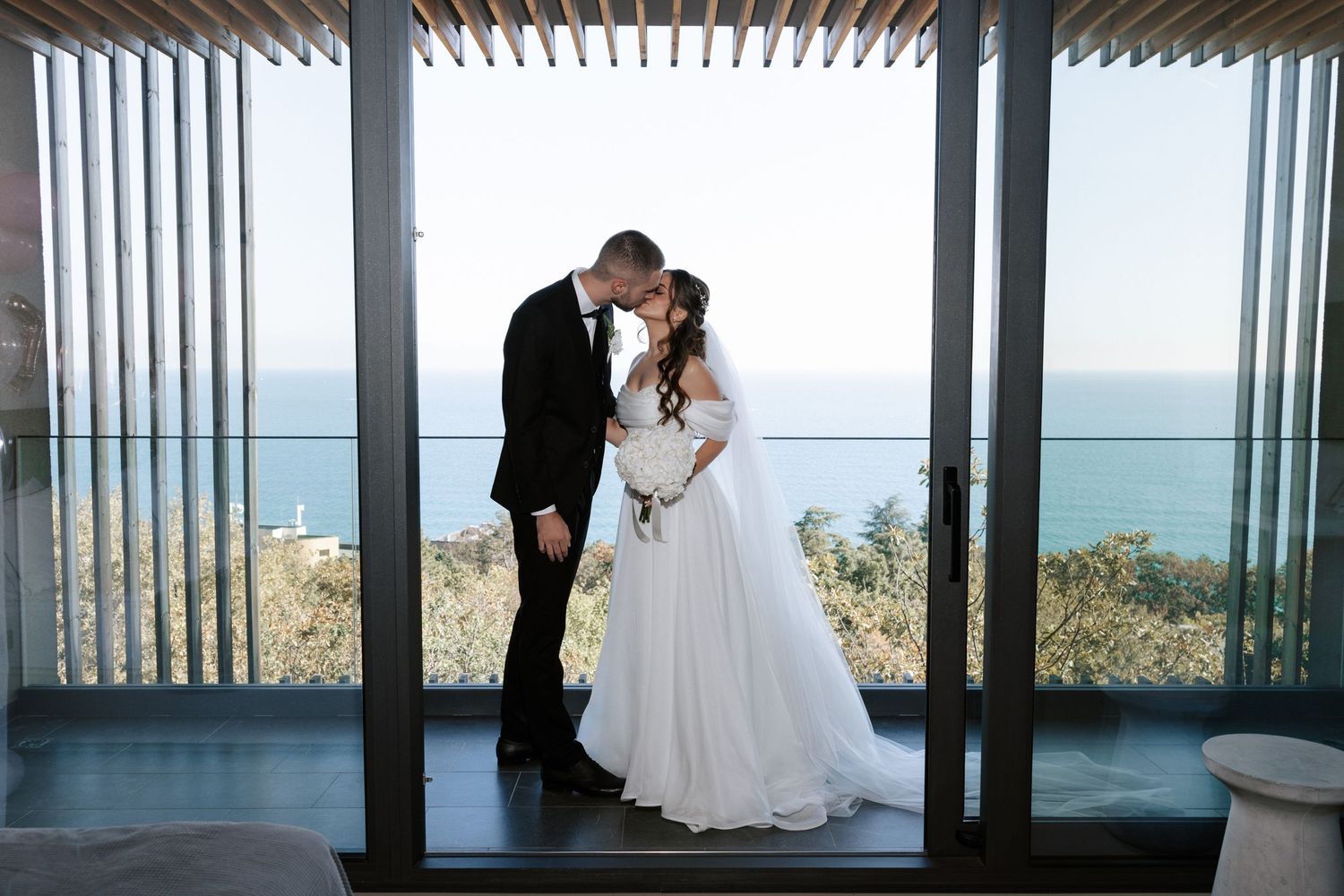 Newlyweds share an intimate moment under a contemporary pergola with ocean views.