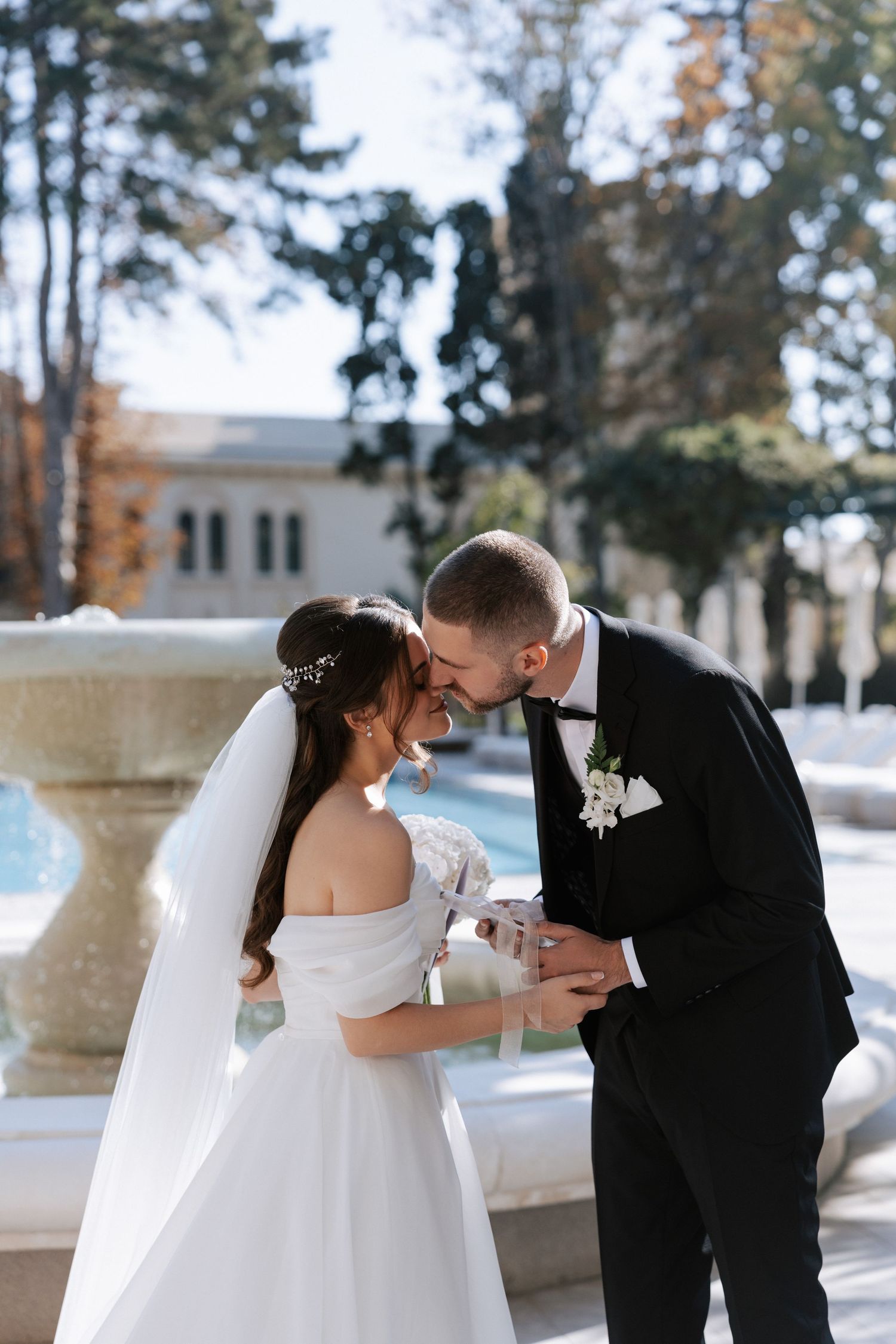 Intimate wedding moment captured by ornate fountain during daytime ceremony.