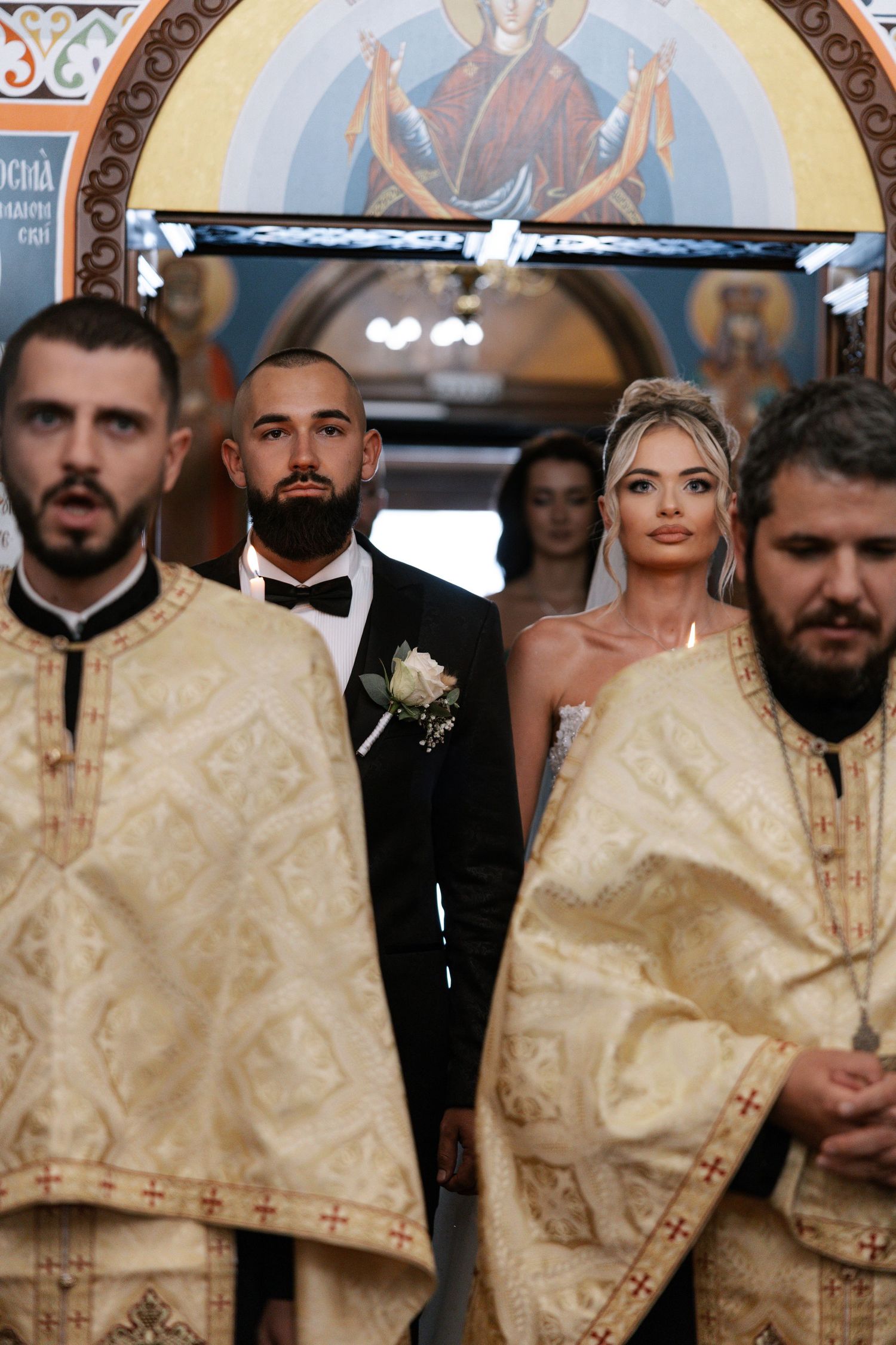 A group of people wearing traditional cream-colored religious vestments stand together during an Orthodox ceremony.