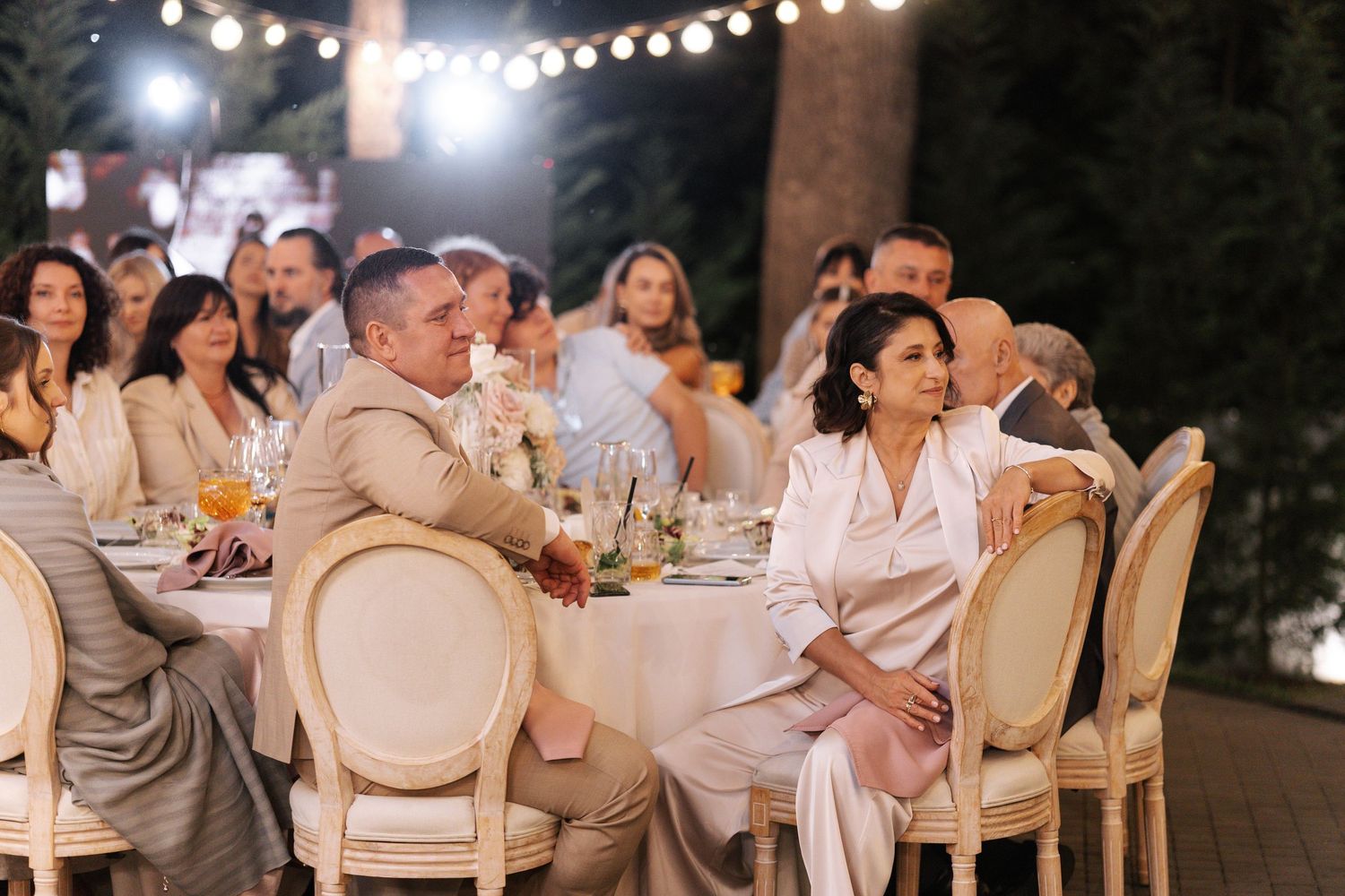 Evening wedding reception with guests seated at elegant tables under ambient lighting.