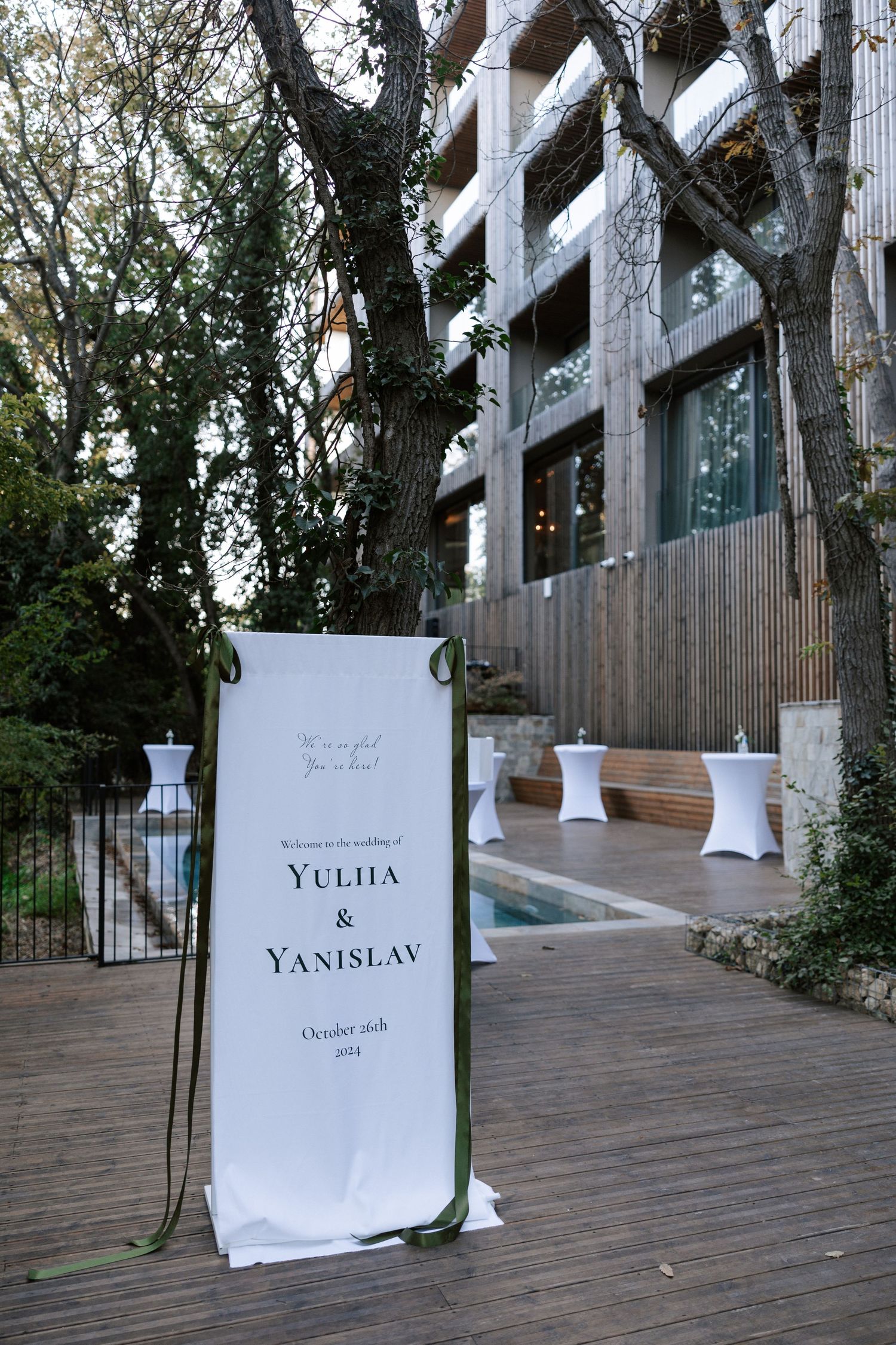Modern wooden building exterior with welcome sign and white cocktail tables on deck.
