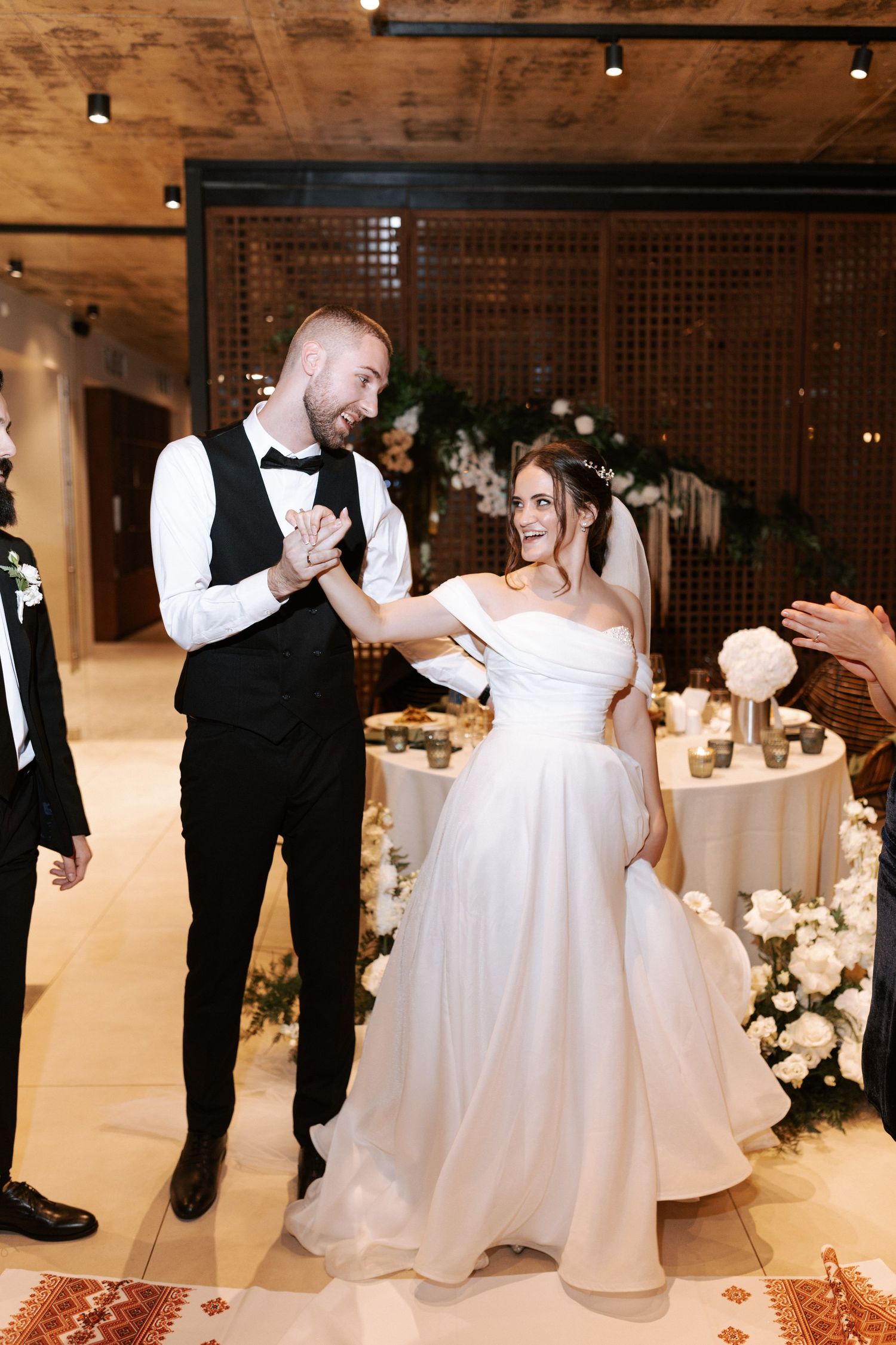 A joyful wedding couple dancing together during their reception beside elegant white floral decorations.