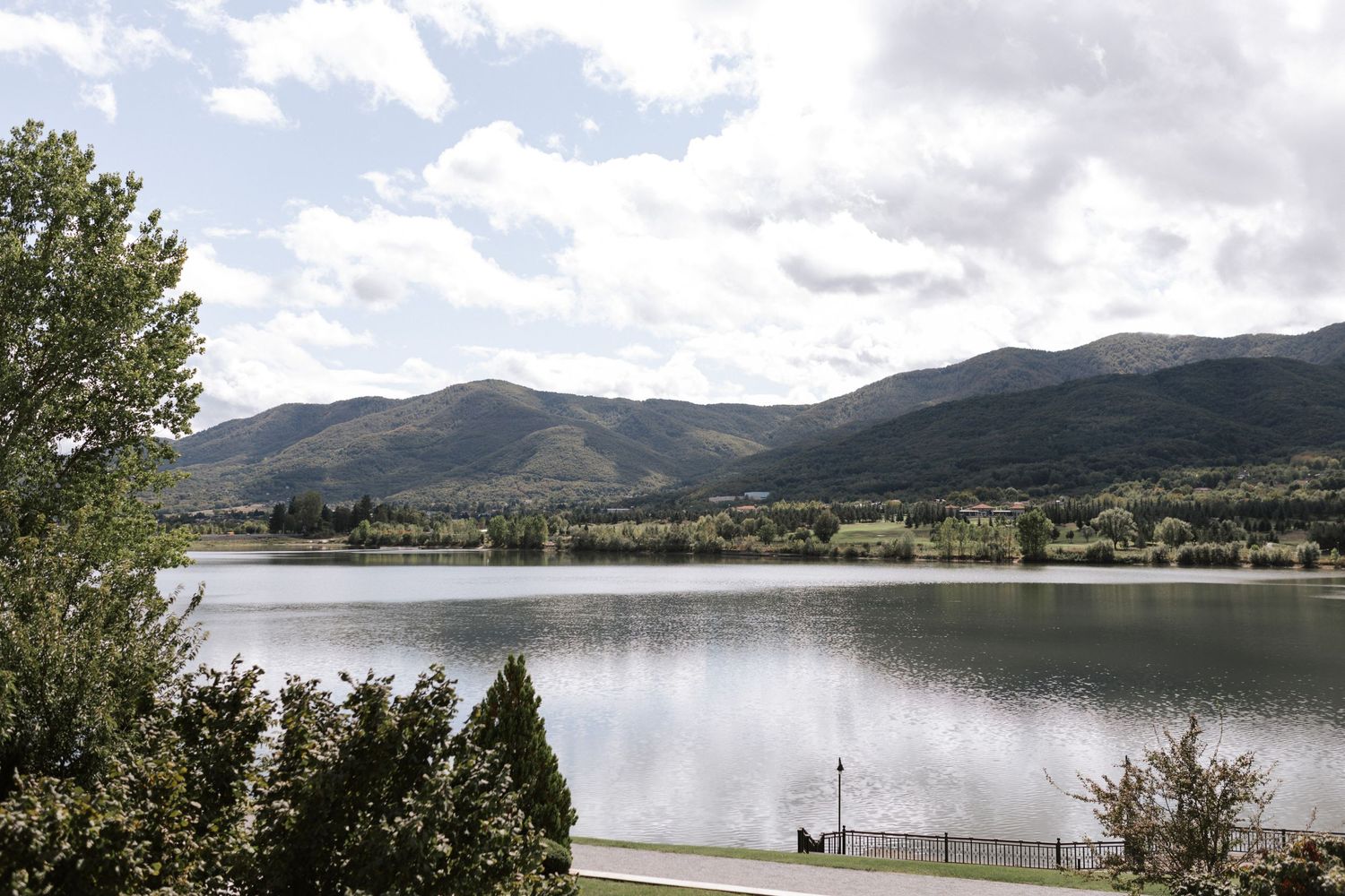 Tranquil mountain lake view with rolling hills and scattered buildings along the shoreline.