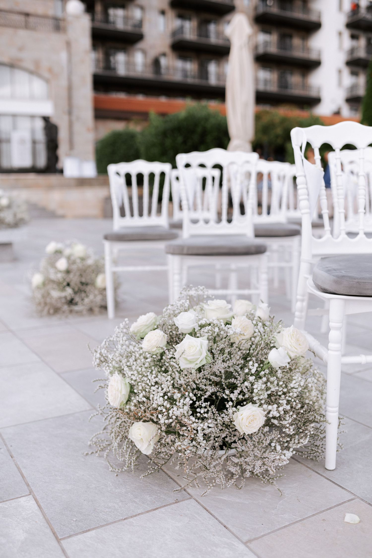 White wedding chairs and baby's breath floral arrangements on outdoor patio.Wedding photographer Bulgaria