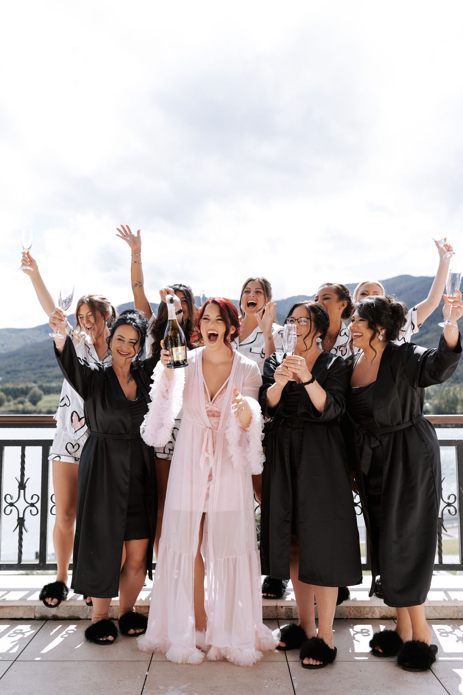 Group celebration on balcony with mountains and lake in background.