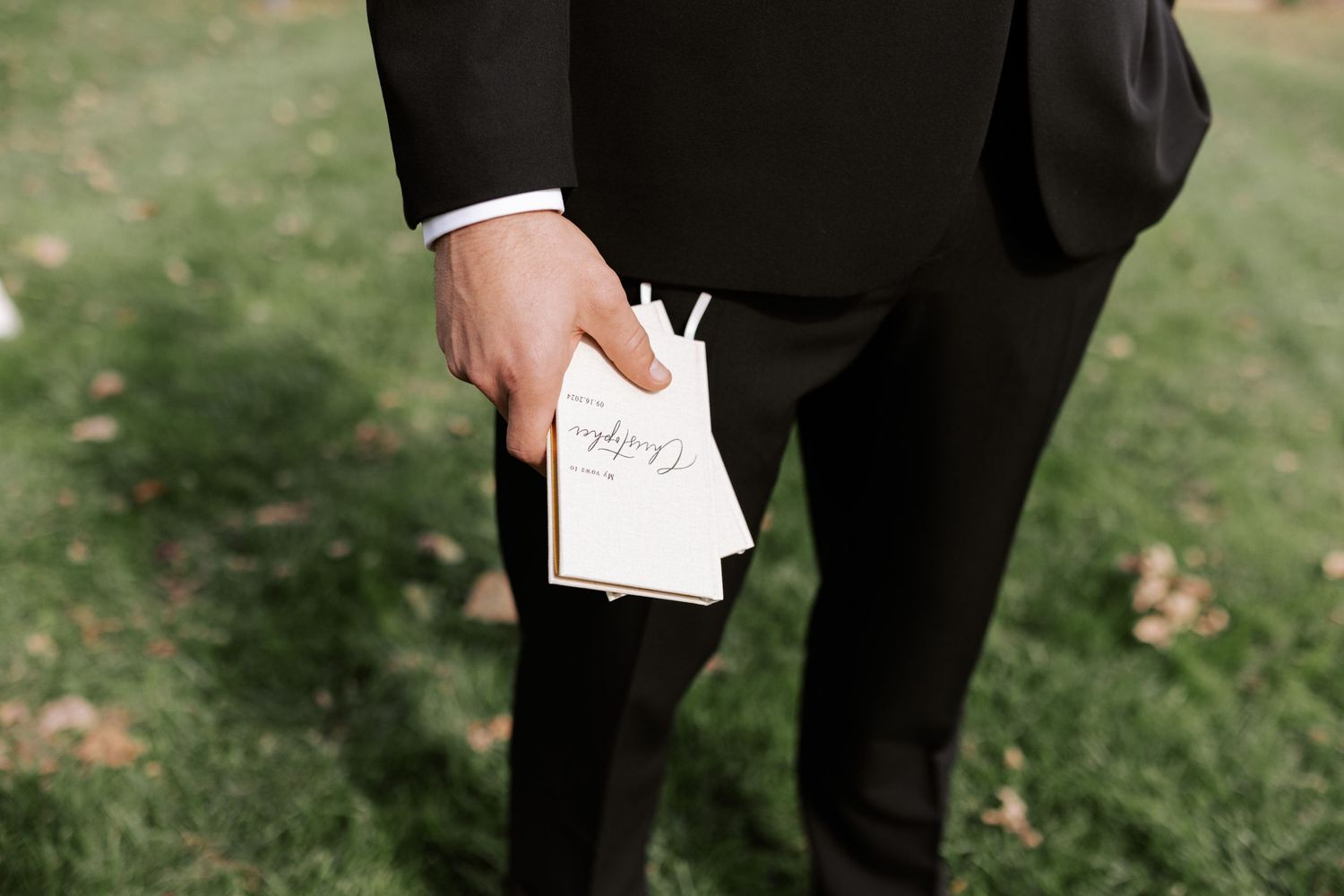 Close-up of someone holding wedding vows written on white paper during an outdoor ceremony.