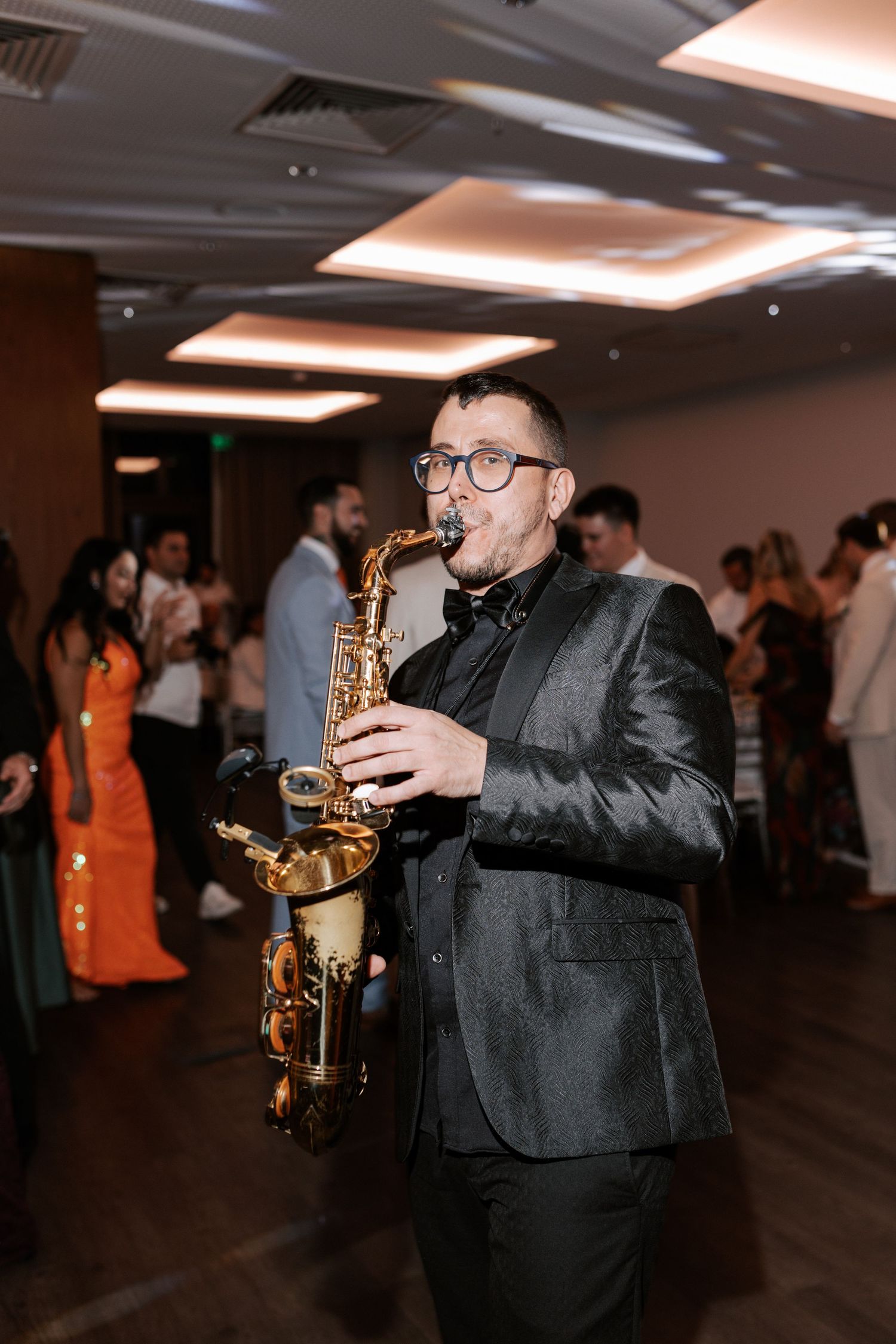 Saxophone player performs wearing black suit during wedding reception.